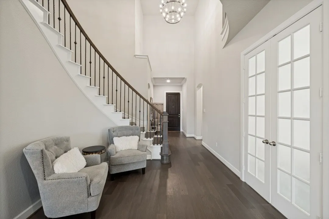 Two-story foyer featuring a curved staircase with wrought iron spindles, dark wood-finish flooring, high ceilings, and double French doors with frosted glass