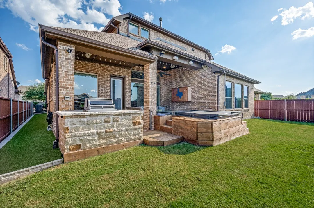 Brick exterior featuring a covered patio with an outdoor grilling station, a tiered wood-finish deck, and an integrated hot tub