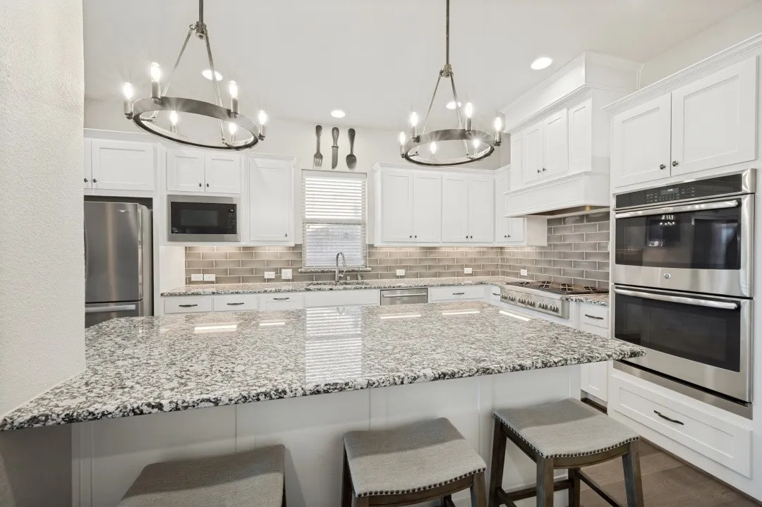 Kitchen featuring a large island with stone countertop, white shaker cabinetry, stainless steel appliances, and a subway tile backsplash