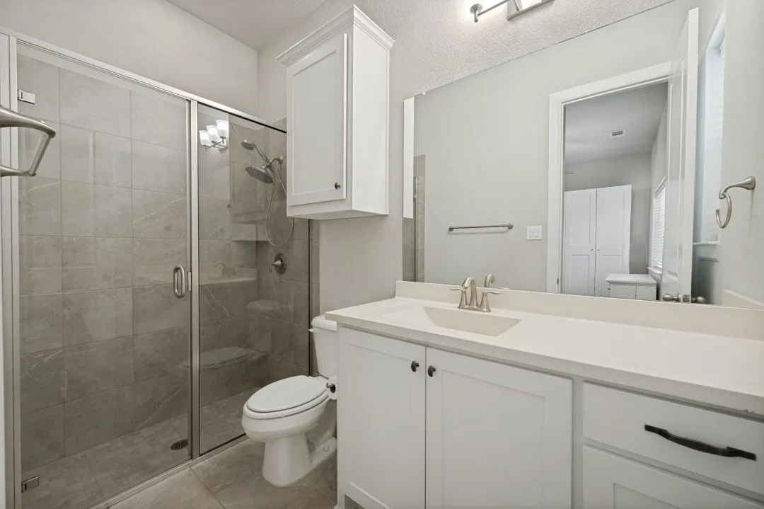 Spacious bathroom featuring a glass-enclosed shower with tile surround, a single vanity with an integrated sink, white cabinetry, and a large wall mirror