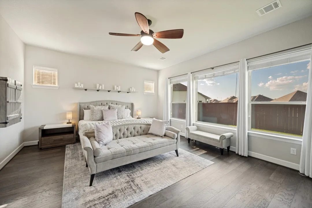 Spacious primary room featuring wood-finish flooring, a ceiling fan, and multiple large windows with blinds
