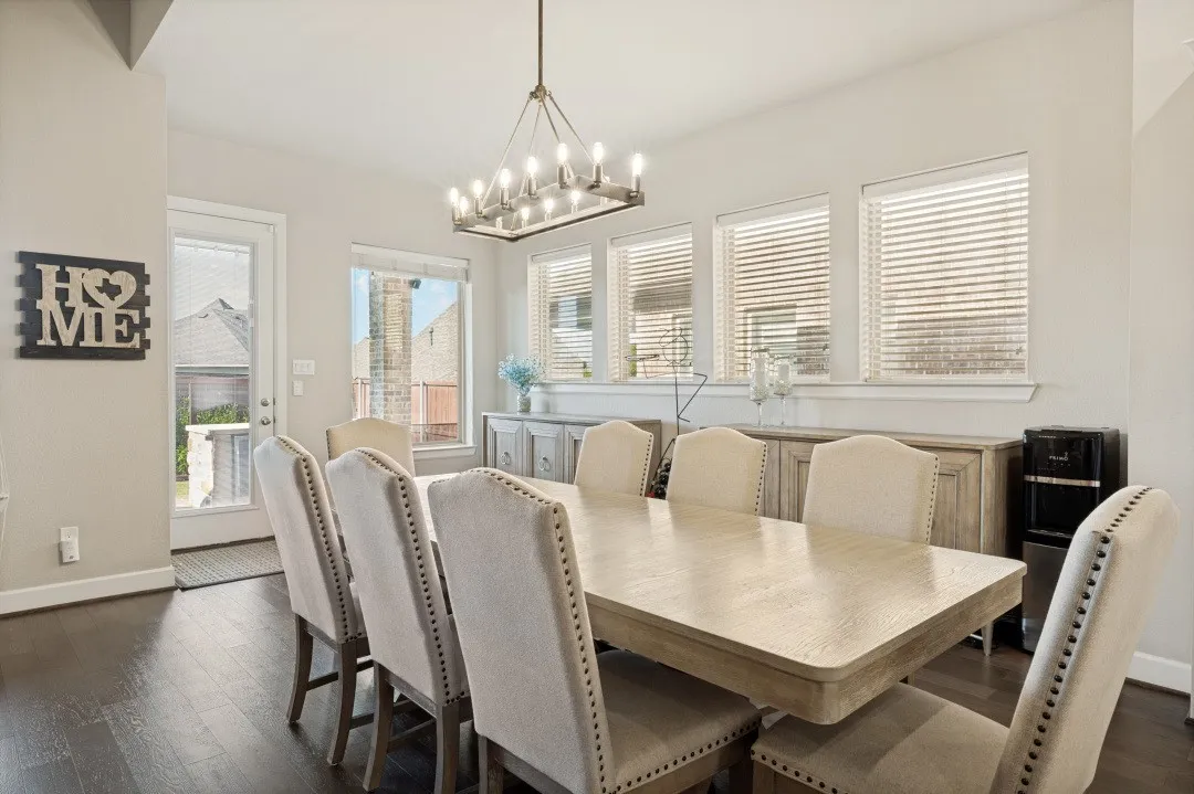Expansive dining room featuring dark wood-finish flooring, light-colored walls, and a contemporary chandelier