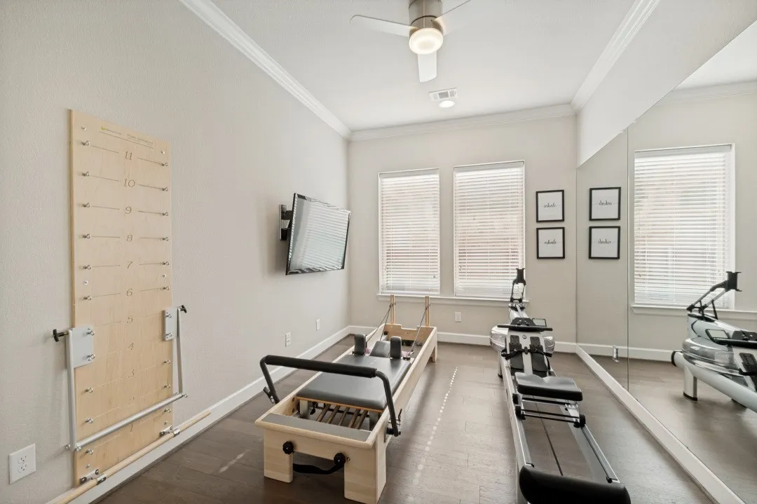 Work out room featuring wood-finish flooring, two windows with blinds, a ceiling fan, and crown molding