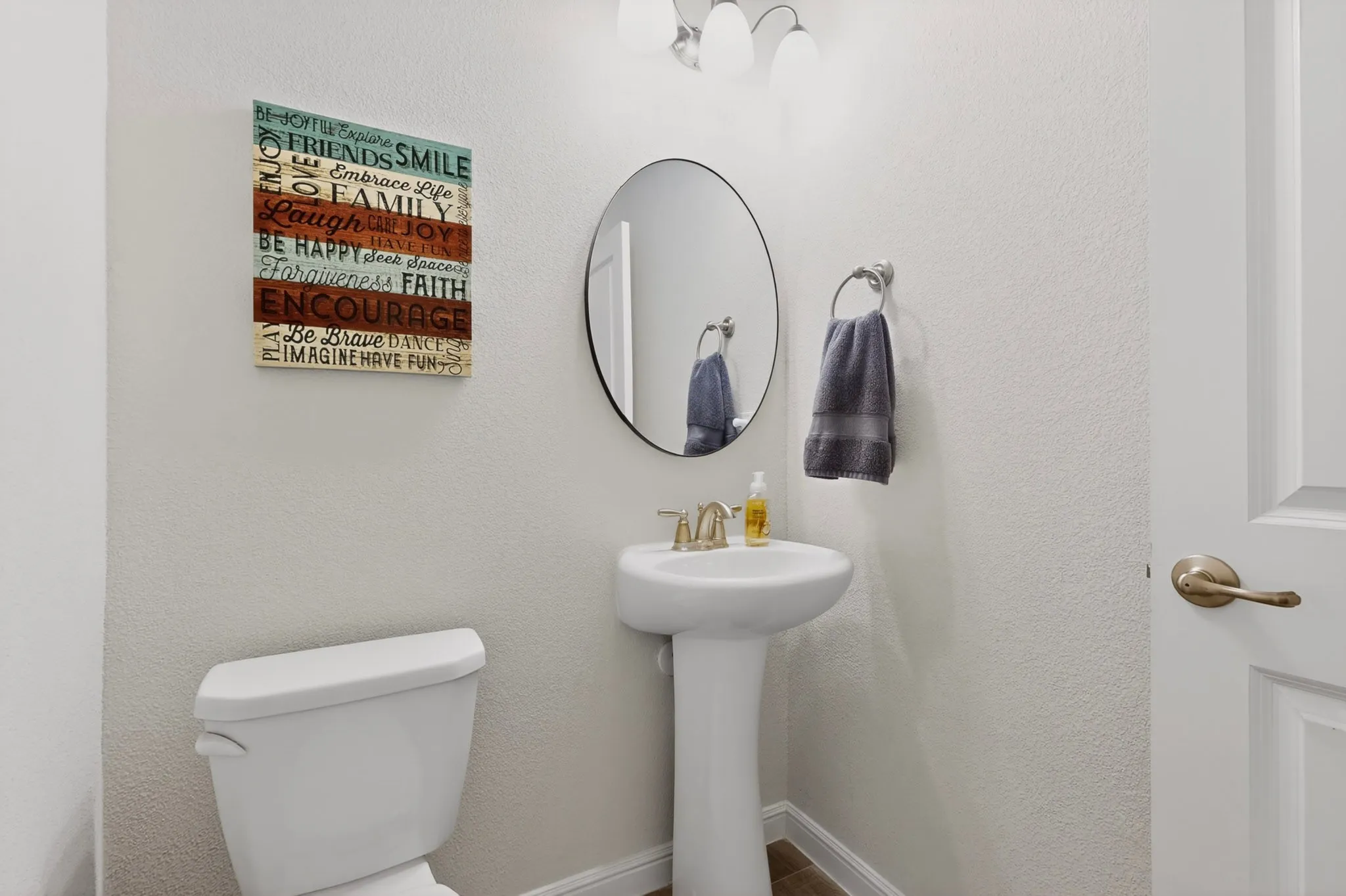 Half Bath White pedestal sink with a bronze-finish faucet, circular framed mirror, and a two-bulb vanity light fixture