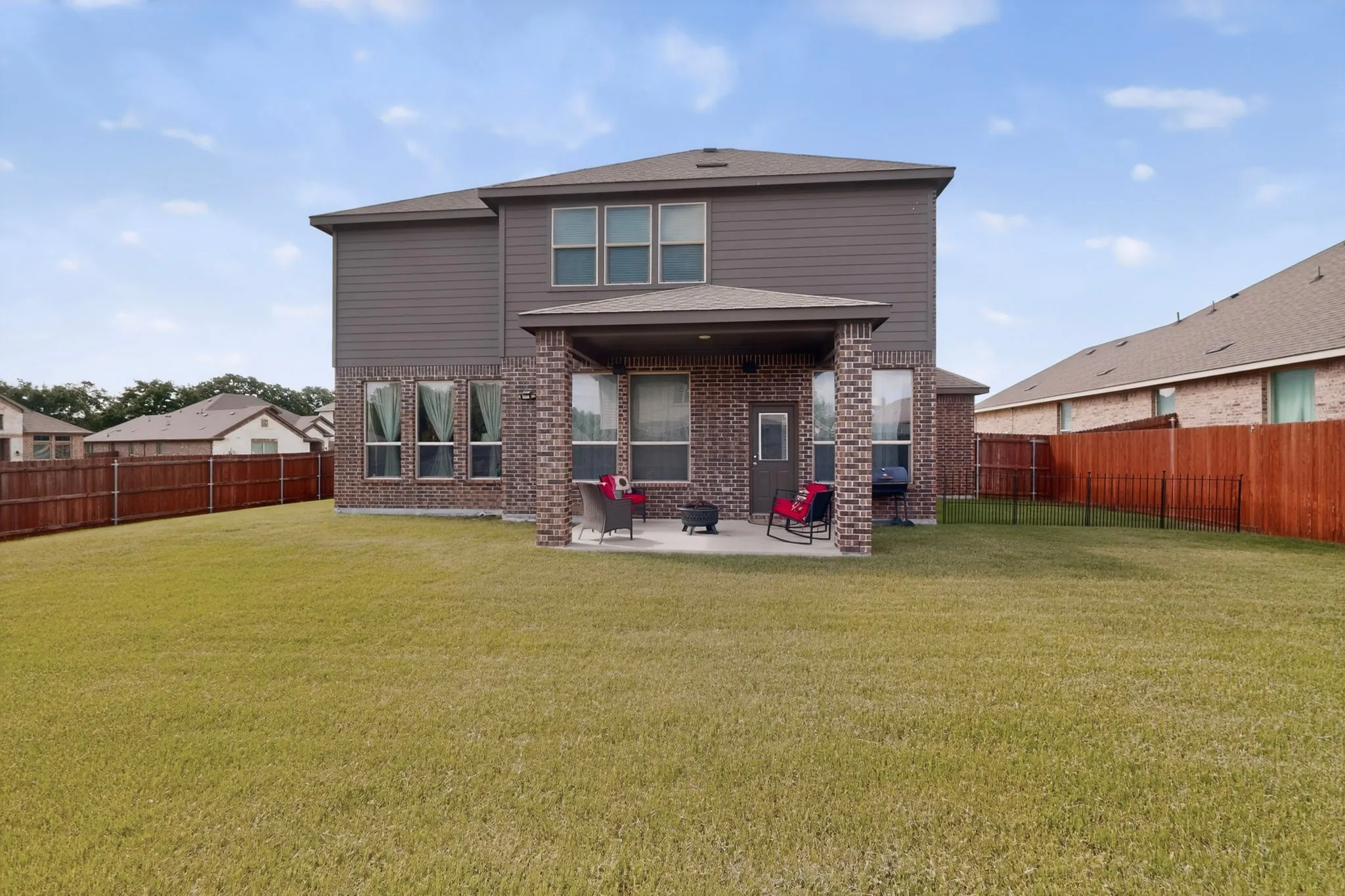 Expansive rear yard featuring a covered patio, brick columns, and a wood fence enclosure