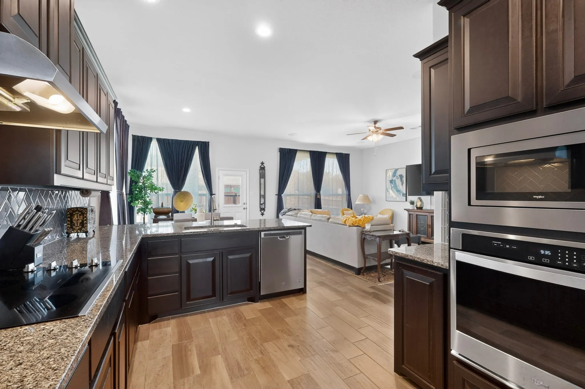 Kitchen featuring dark wood cabinetry, granite countertops, an integrated cooktop, and built-in stainless steel appliances