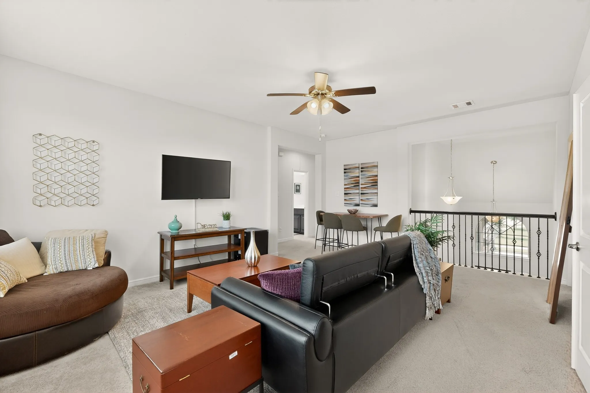 Open-concept loft space featuring light-colored carpeting, a brass-finish ceiling fan, and a built-in wrought iron railing overlooking the lower level