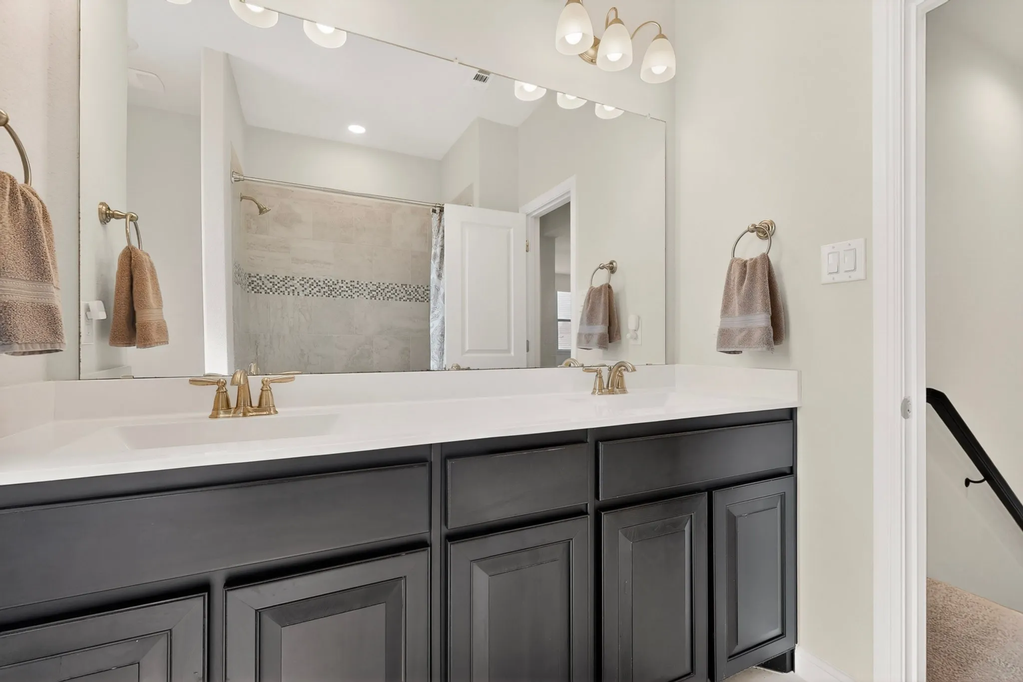 Dual vanity featuring dark cabinetry, white countertops, and brass-finish fixtures