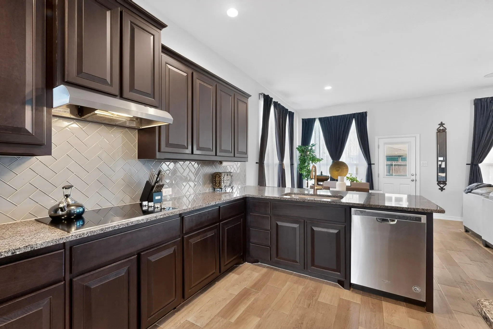Kitchen featuring dark wood cabinetry, granite countertops, herringbone tile backsplash, stainless steel appliances, and wood-finish flooring