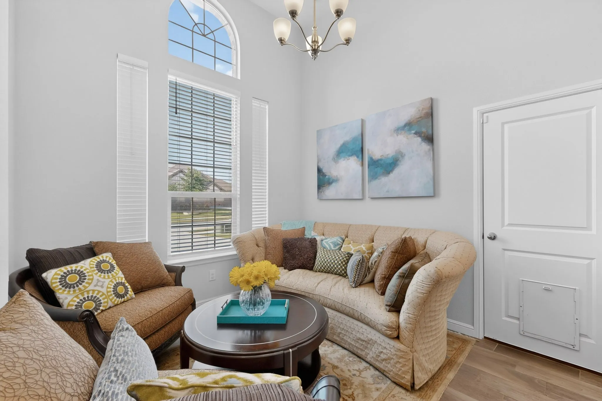 Living area featuring wood-finish flooring, a contemporary chandelier, high ceilings, and an arched transom window
