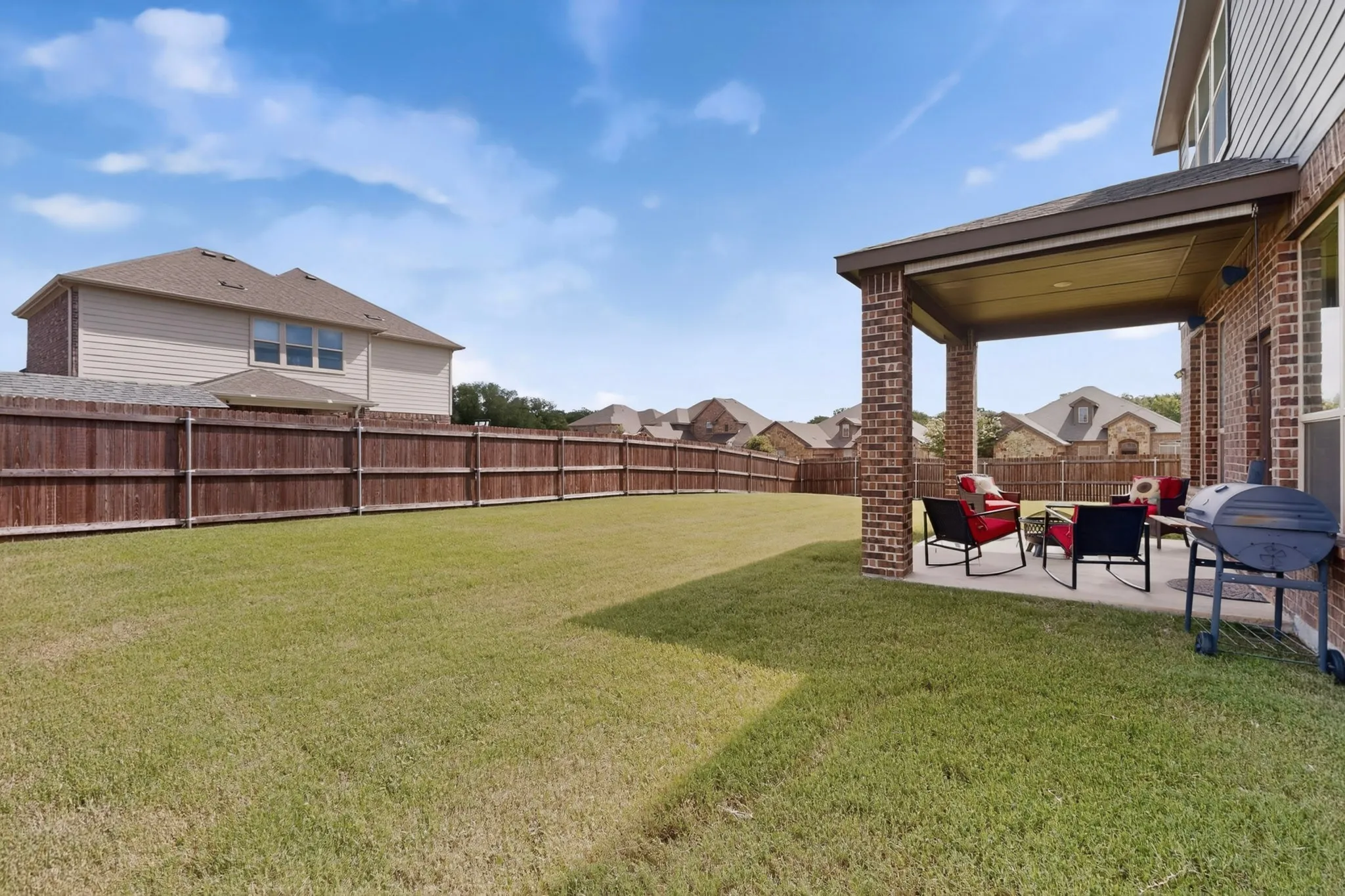 Expansive backyard featuring a covered patio, brick columns, concrete flooring, and a full wood fence