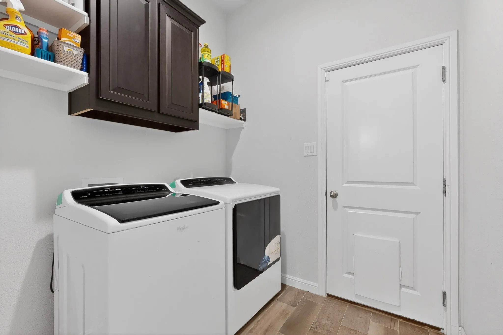 Laundry room featuring wood-finish flooring, white walls, and a white paneled door
