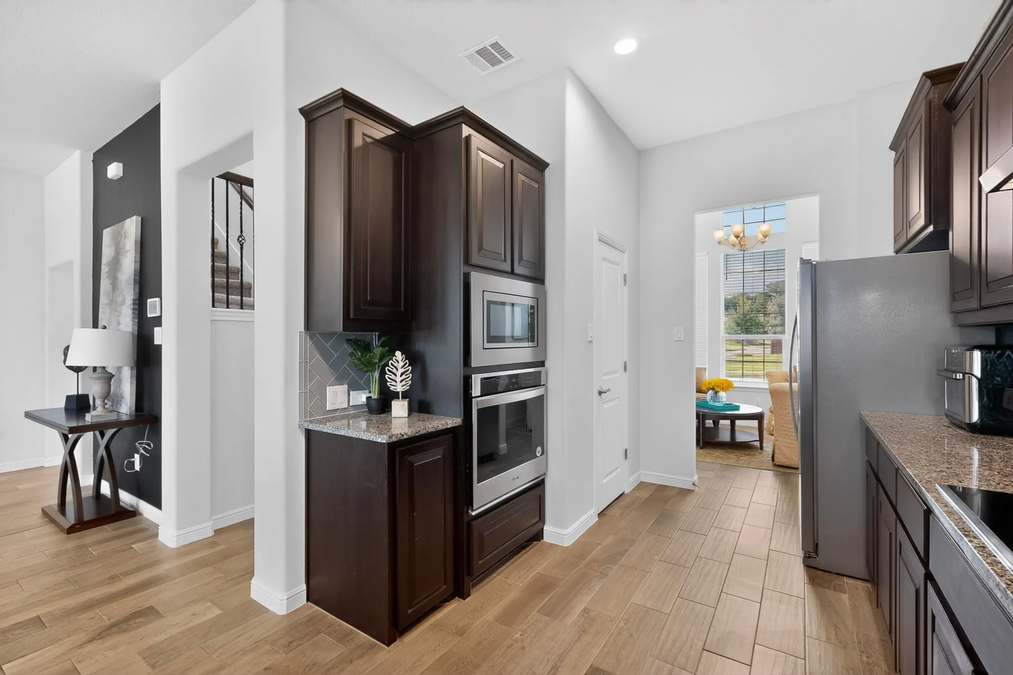 Kitchen featuring wood-finish tile flooring, dark wood cabinetry, stainless steel built-in microwave and oven, and granite-style countertops