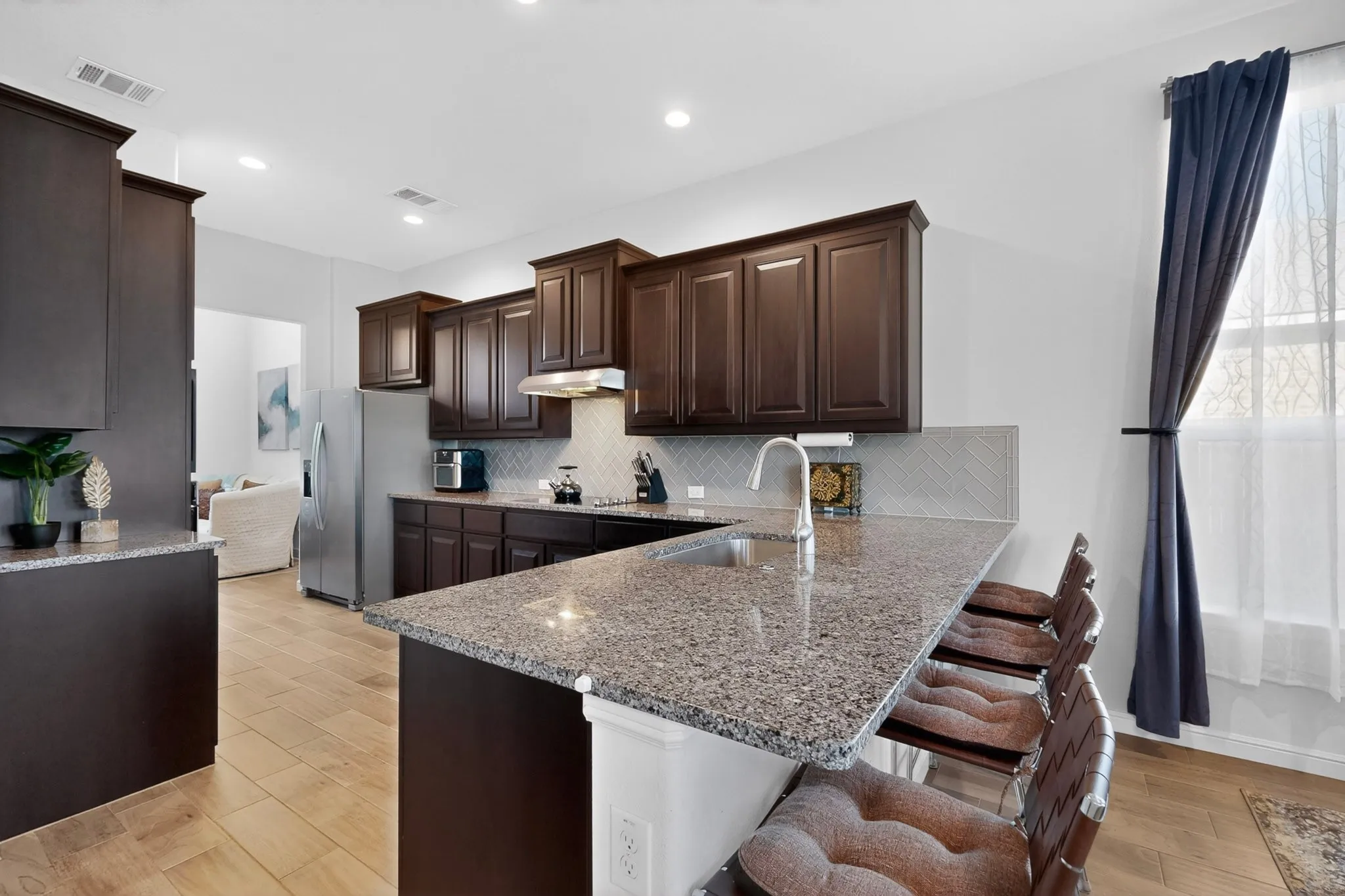 Kitchen featuring granite countertops, wood-finish flooring, dark wood cabinetry, a stainless steel refrigerator, and a stainless steel sink with a gooseneck faucet