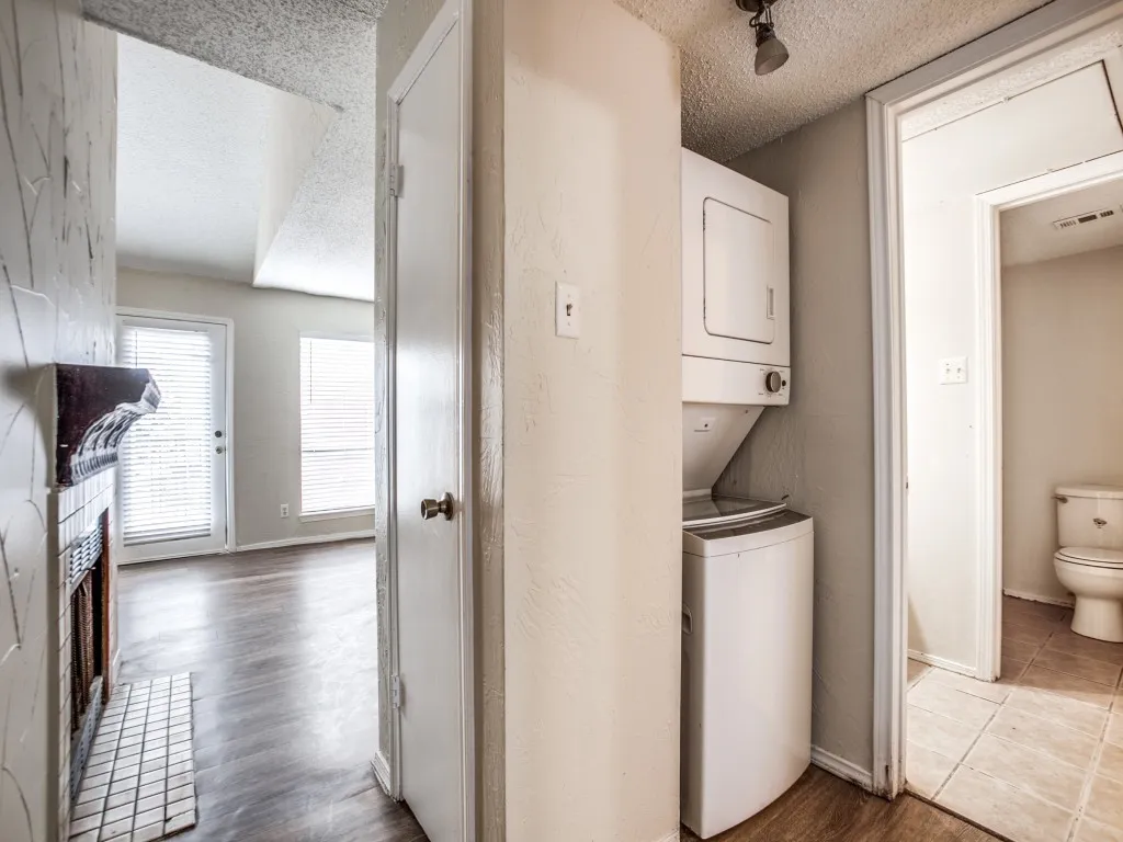 Clothes washing area with light hardwood / wood-style floors, stacked washer and dryer, and a textured ceiling