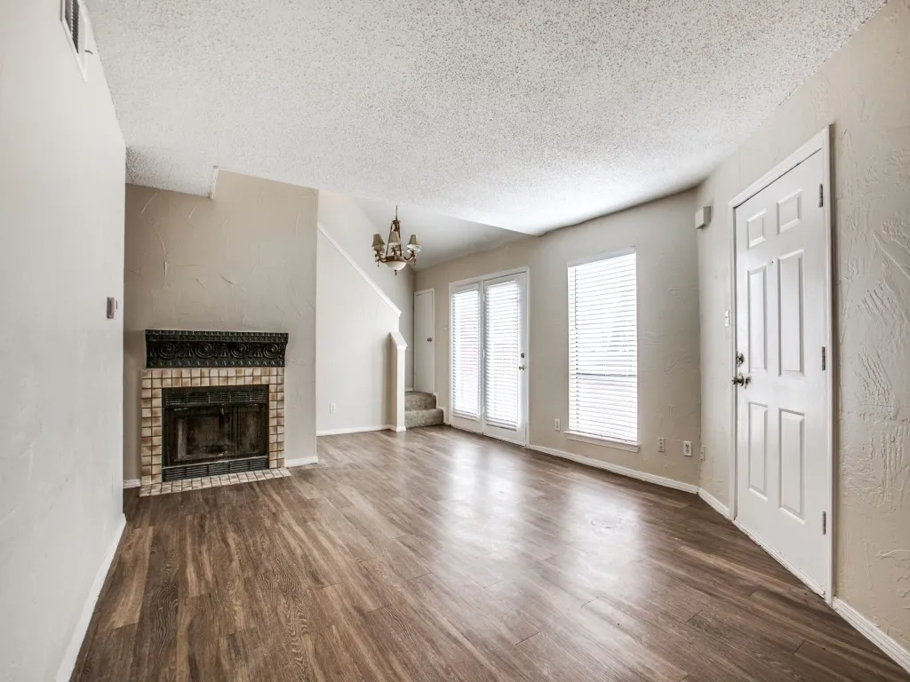 Unfurnished living room with a fireplace, a textured ceiling, an inviting chandelier, and dark wood-type flooring