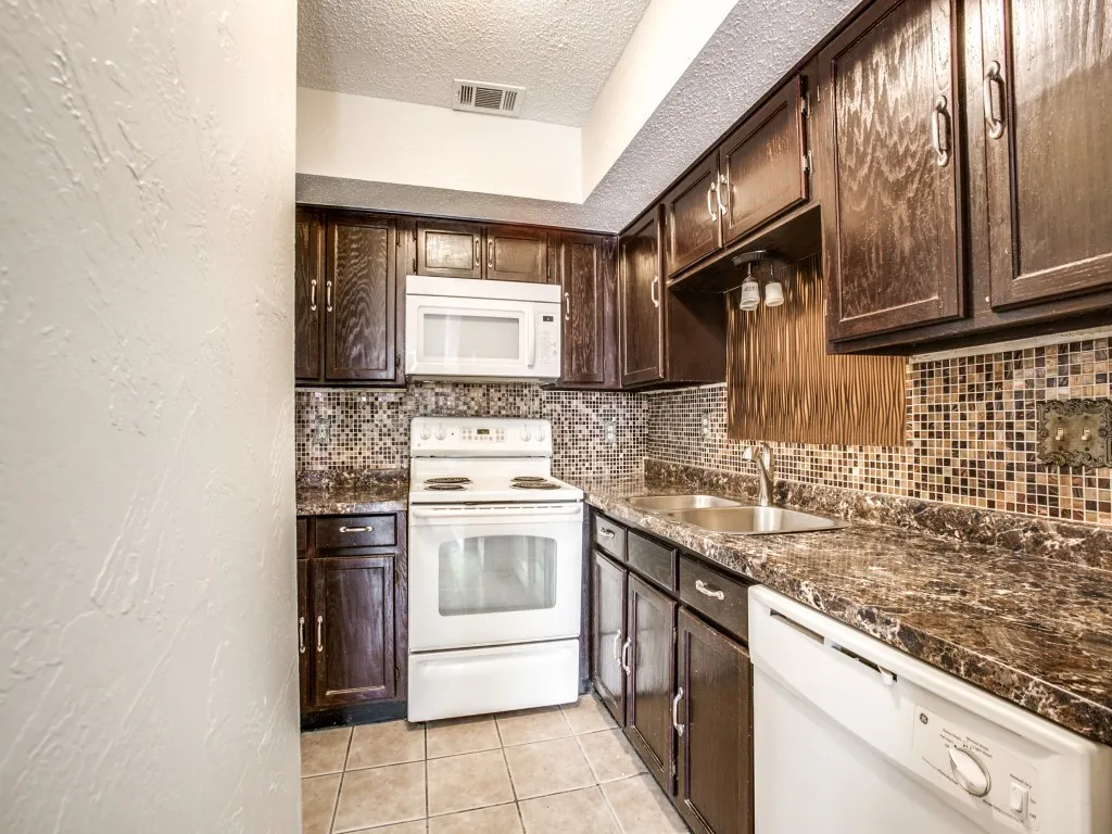 Kitchen featuring backsplash, sink, a textured ceiling, light tile patterned floors, and white appliances