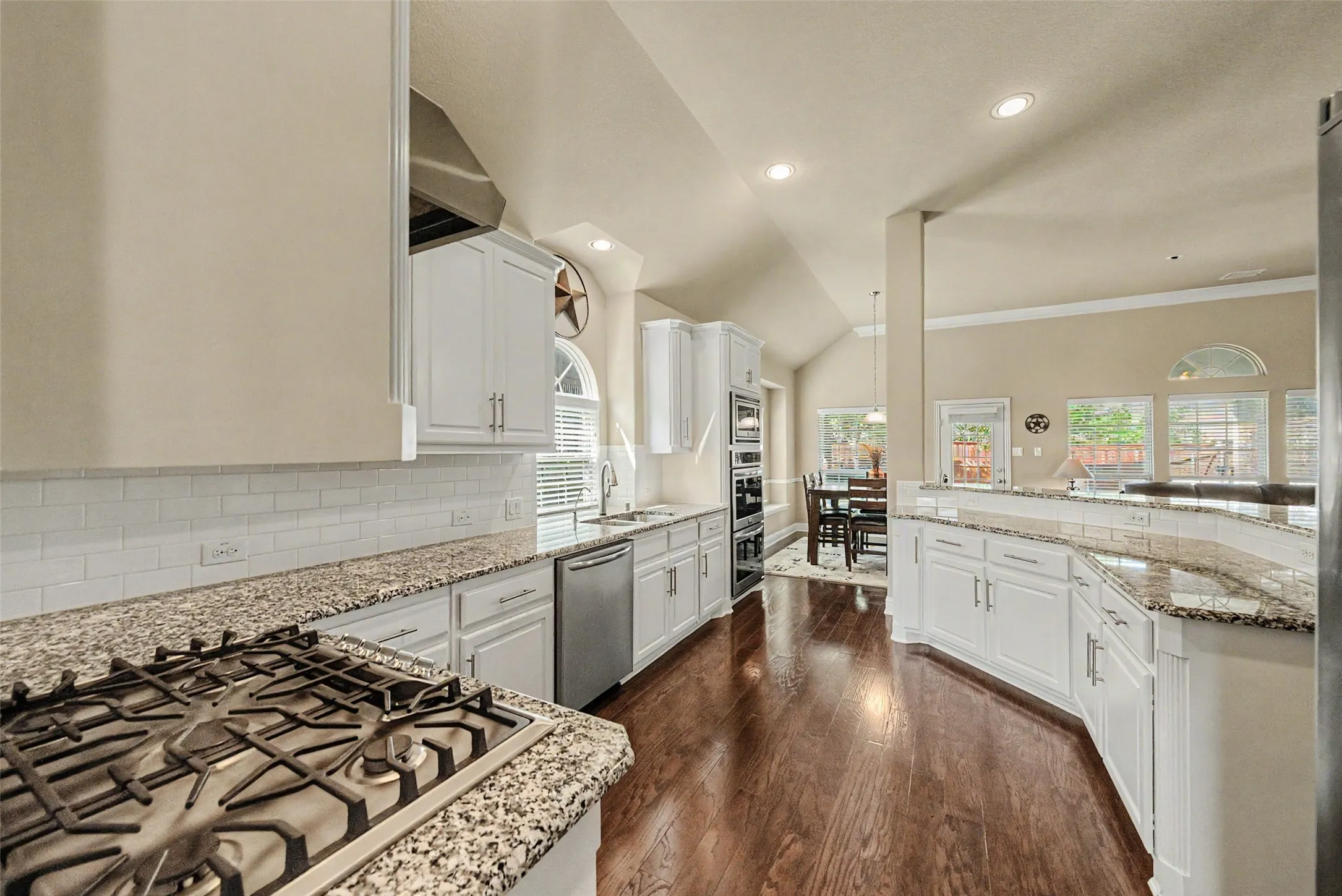 Kitchen featuring white cabinetry, granite countertops, wood-finish flooring, stainless steel appliances, and a subway tile backsplash