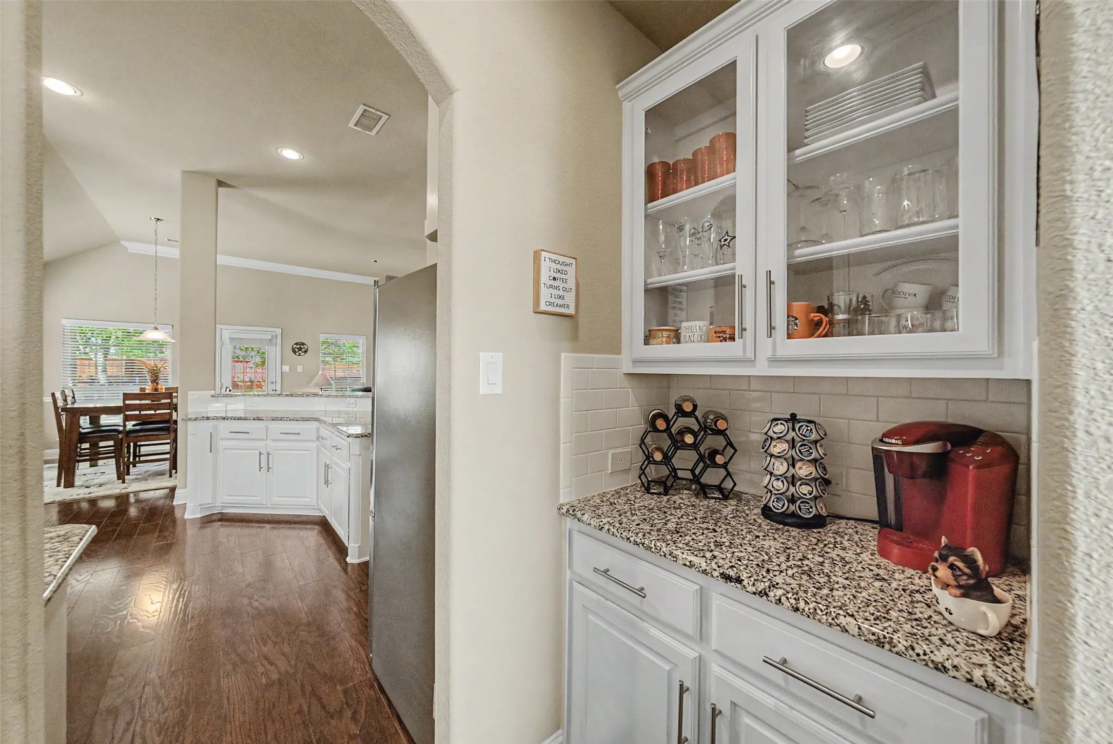 Kitchen featuring white cabinetry, granite-style countertops, subway tile backsplash, and glass-front upper cabinets