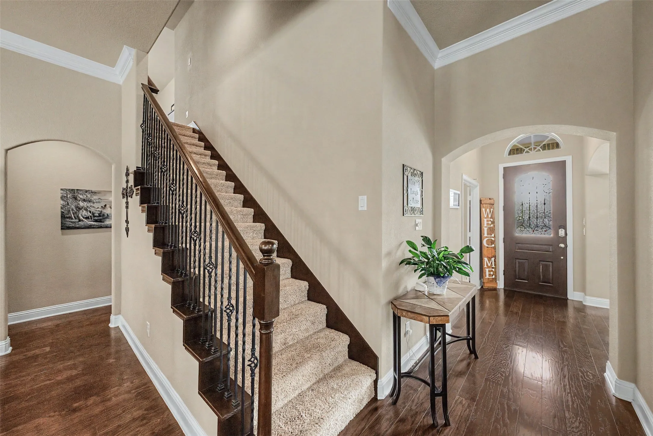 Foyer featuring a grand staircase with wrought iron balusters and a dark wood handrail, high ceilings, arched doorways, and rich wood-finish flooring