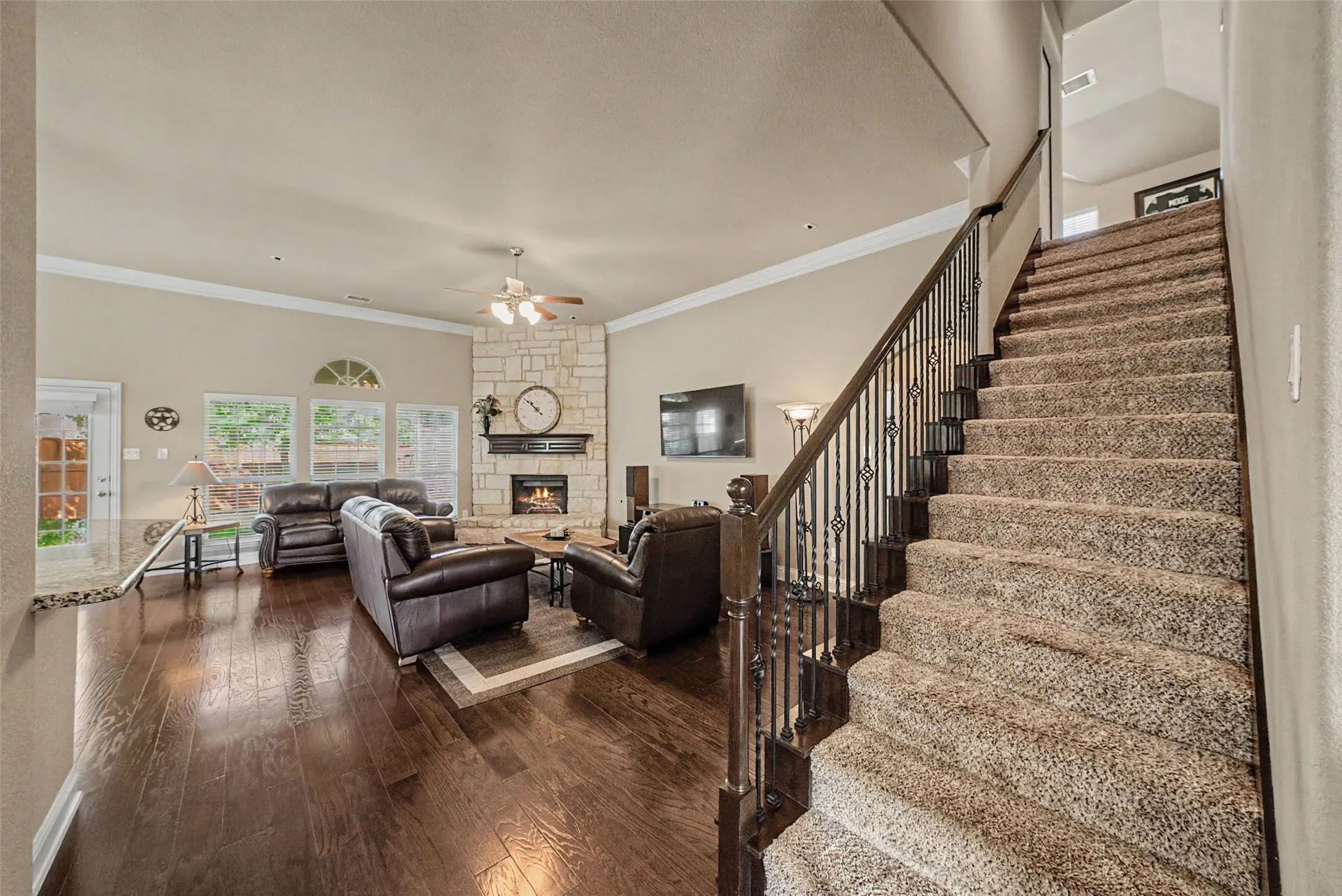 Spacious common area featuring wood-finish flooring, a stone-clad fireplace, and multiple windows