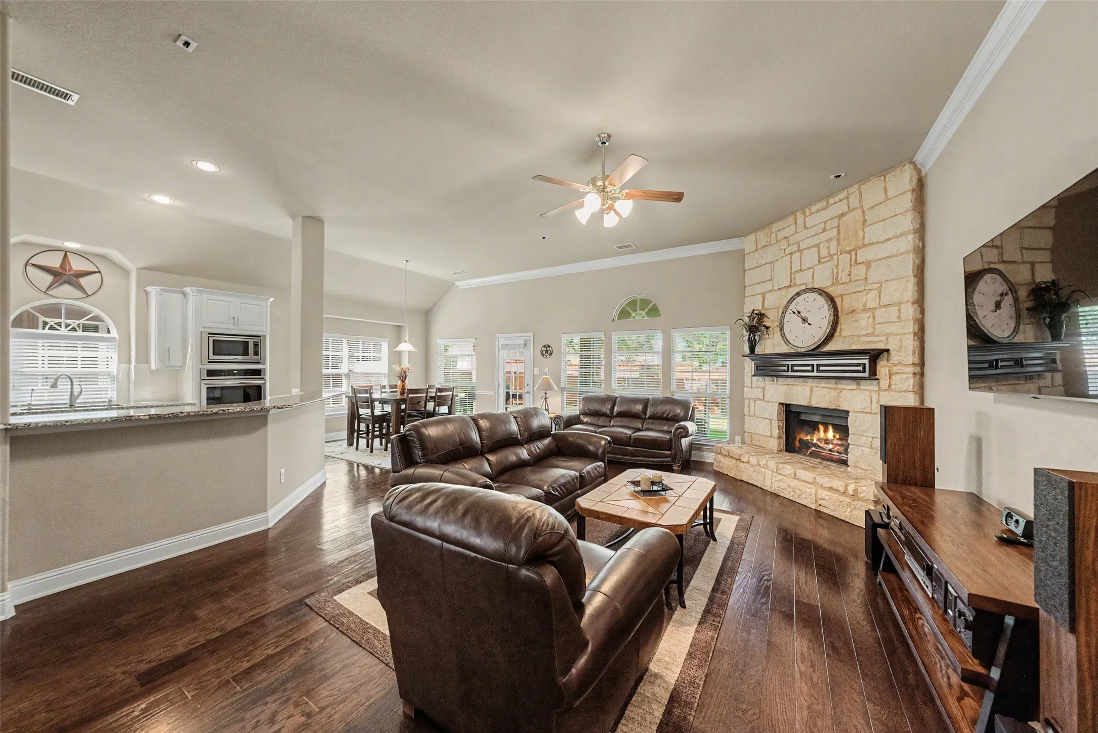 Spacious living area featuring wood-finish flooring, a stone fireplace with hearth and mantel, and vaulted ceilings