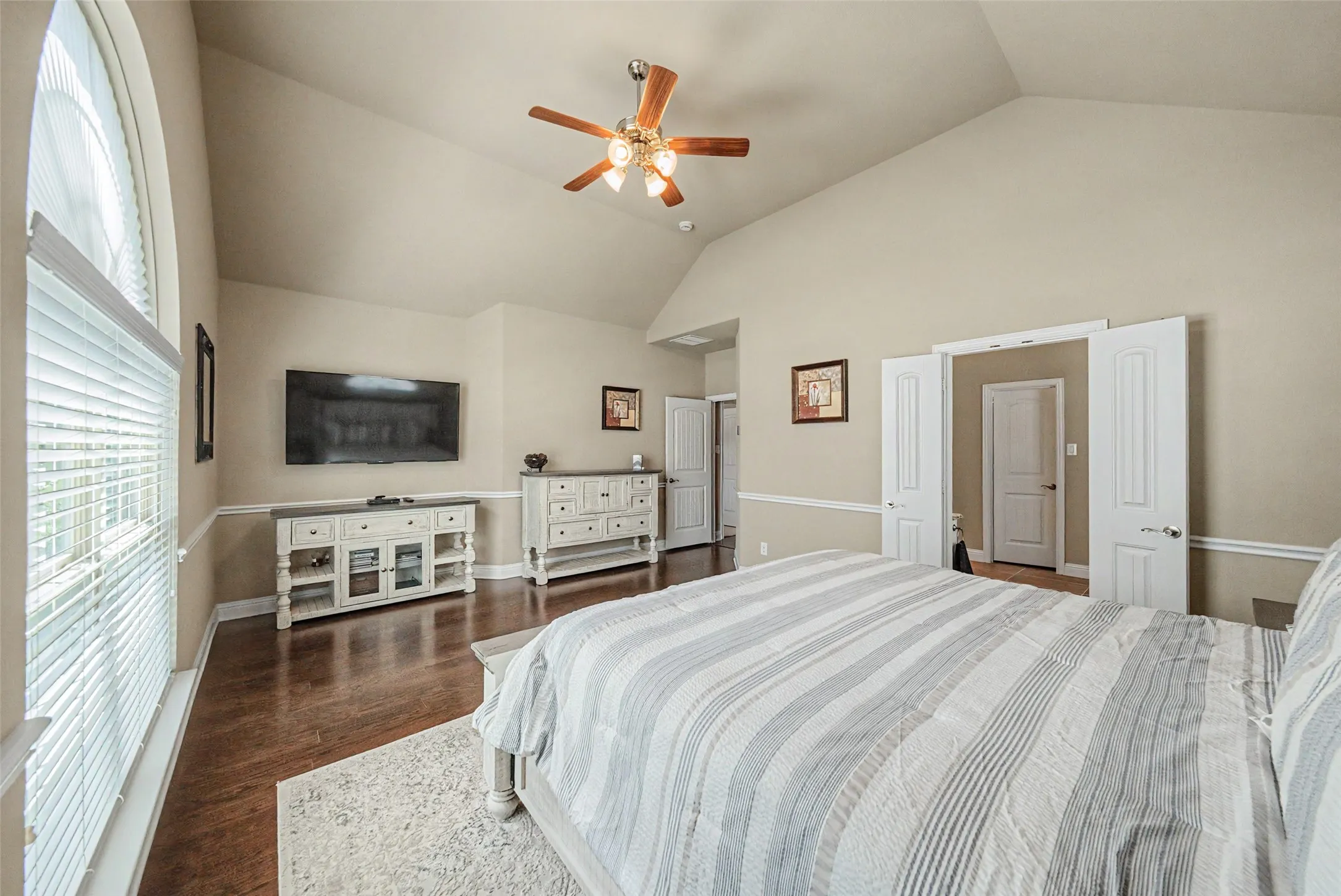 Vaulted ceilings in this room featuring wood-finish flooring, a large arched window with blinds, and a ceiling fan with integrated lighting