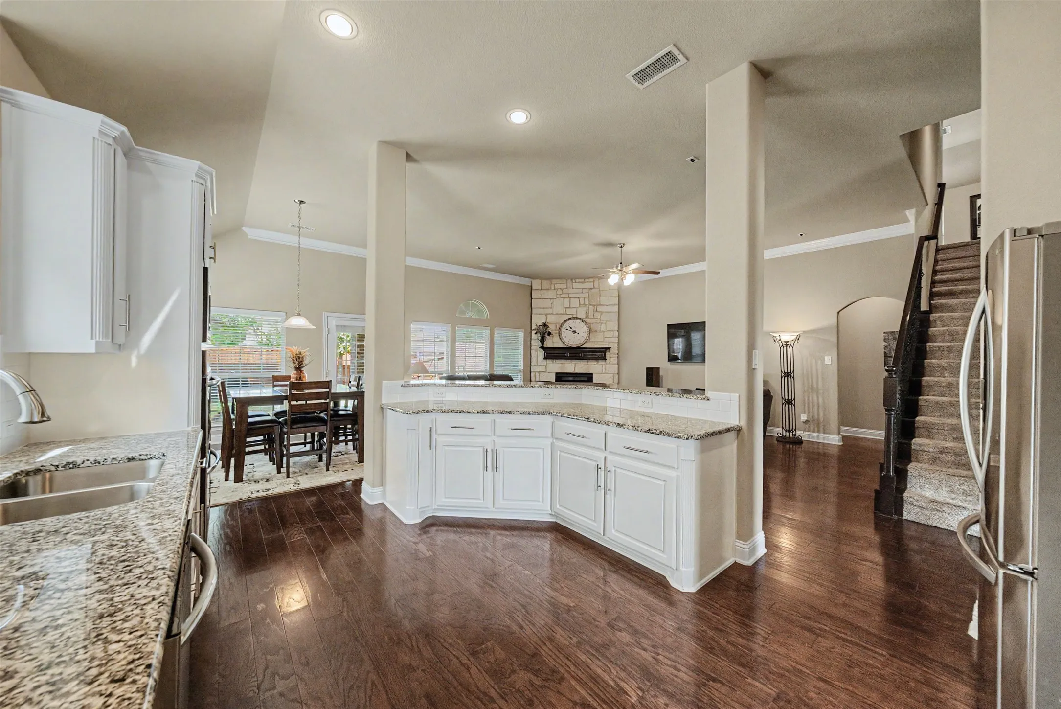 Open-concept interior featuring wood-finish flooring, white cabinetry, granite countertops, and recessed lighting