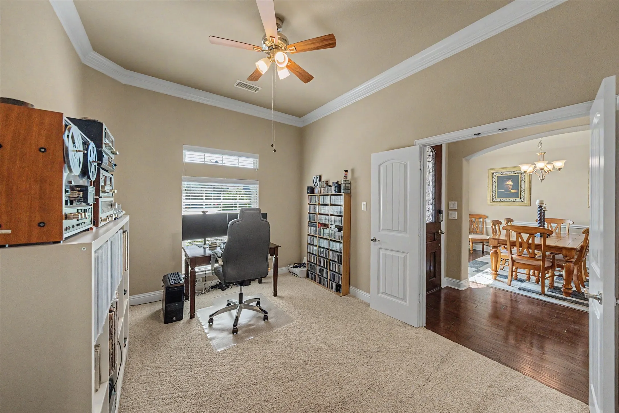 Carpeted room with a ceiling fan, crown molding, and an arched entryway featuring wood-finish flooring