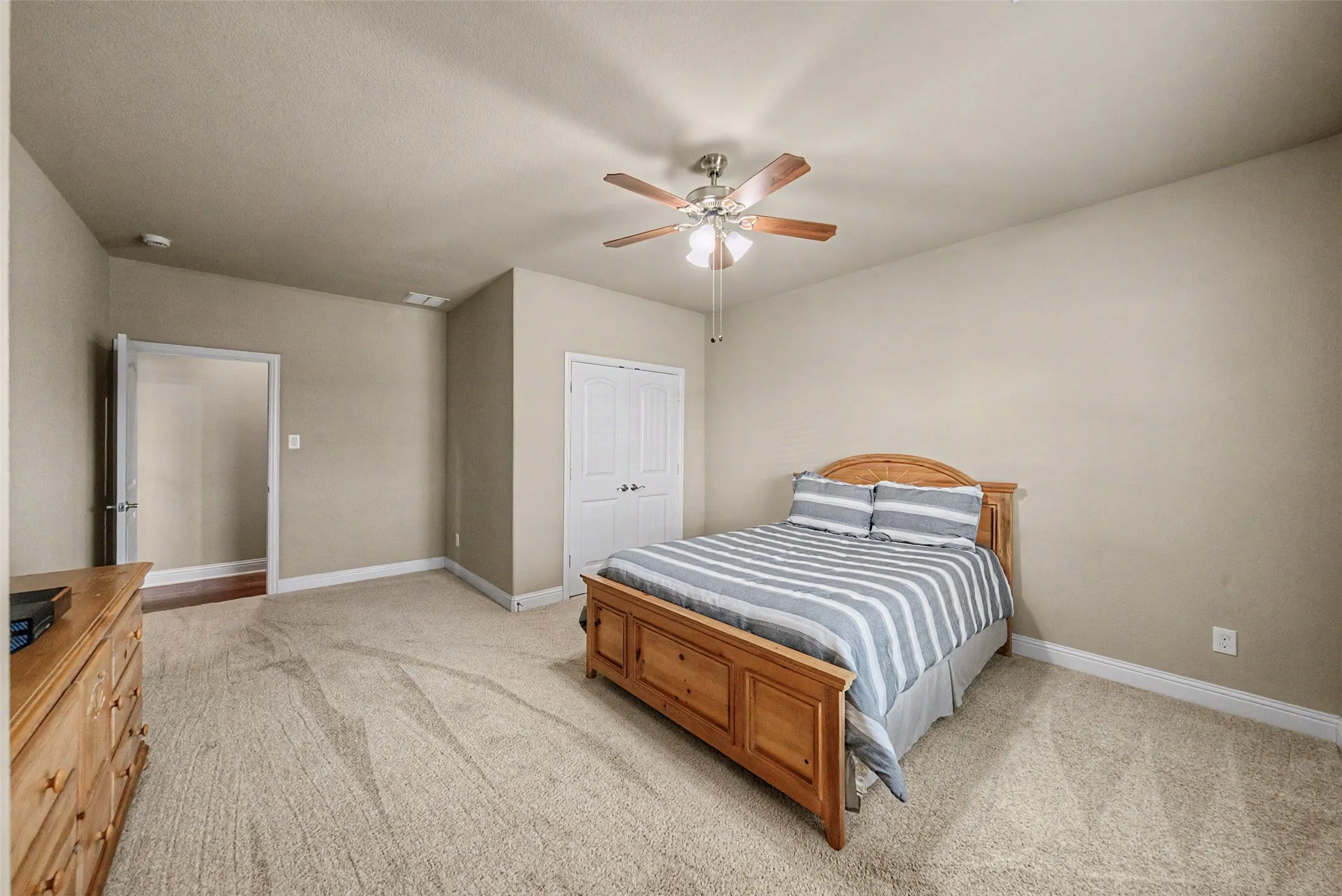 Spacious room featuring neutral wall tones, textured carpeting, a ceiling fan with light fixture, white trim, and a white bi-fold closet door