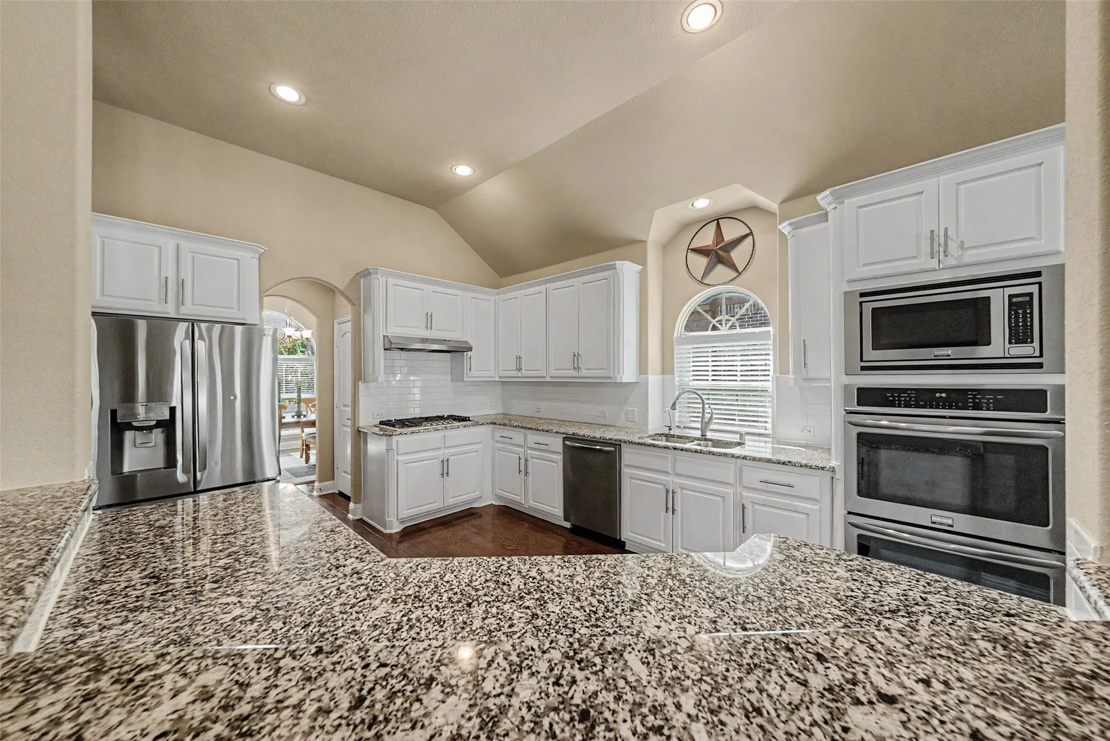 Kitchen featuring white cabinetry with brushed nickel hardware, speckled granite countertops, and a subway tile backsplash