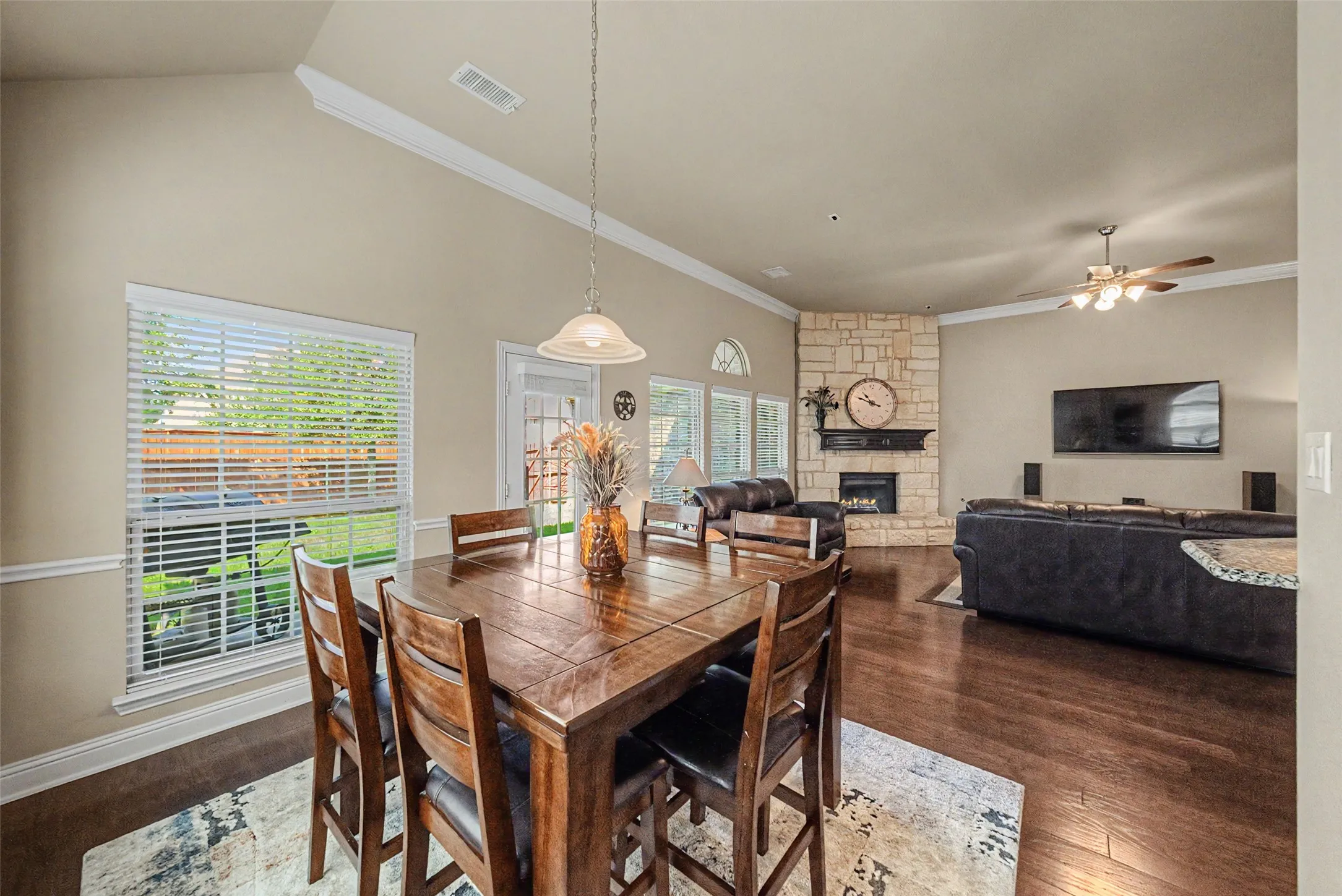 Open-concept living space featuring wood-finish flooring, a vaulted ceiling, and a stone-clad fireplace