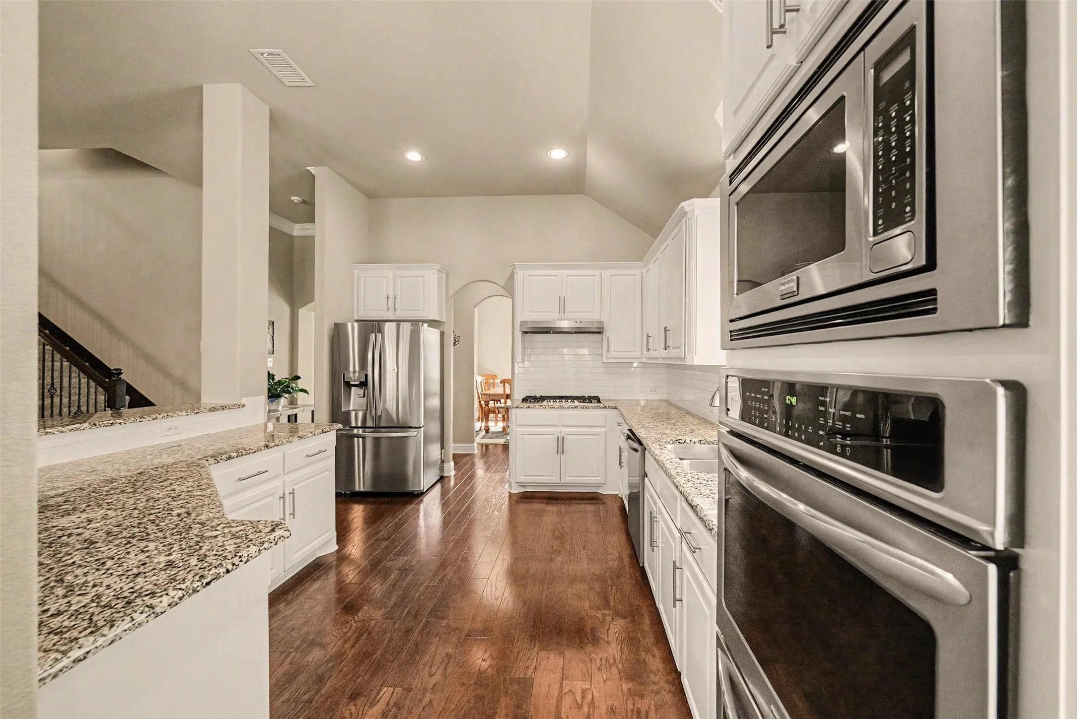 Expansive kitchen featuring granite countertops, white cabinetry, stainless steel appliances, wood-finish flooring, and recessed lighting