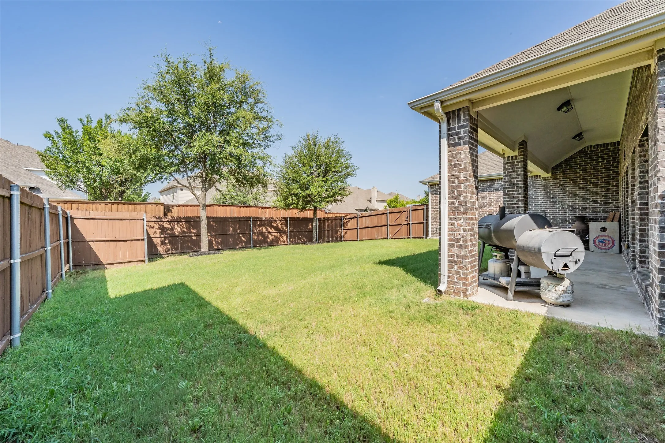 Expansive backyard featuring a lush lawn and a covered patio with brick columns