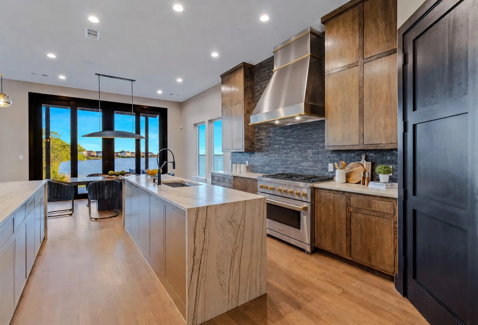 Gourmet kitchen with wood-finish flooring, a large island featuring a waterfall edge, and a professional-grade stainless steel range with a coordinating hood