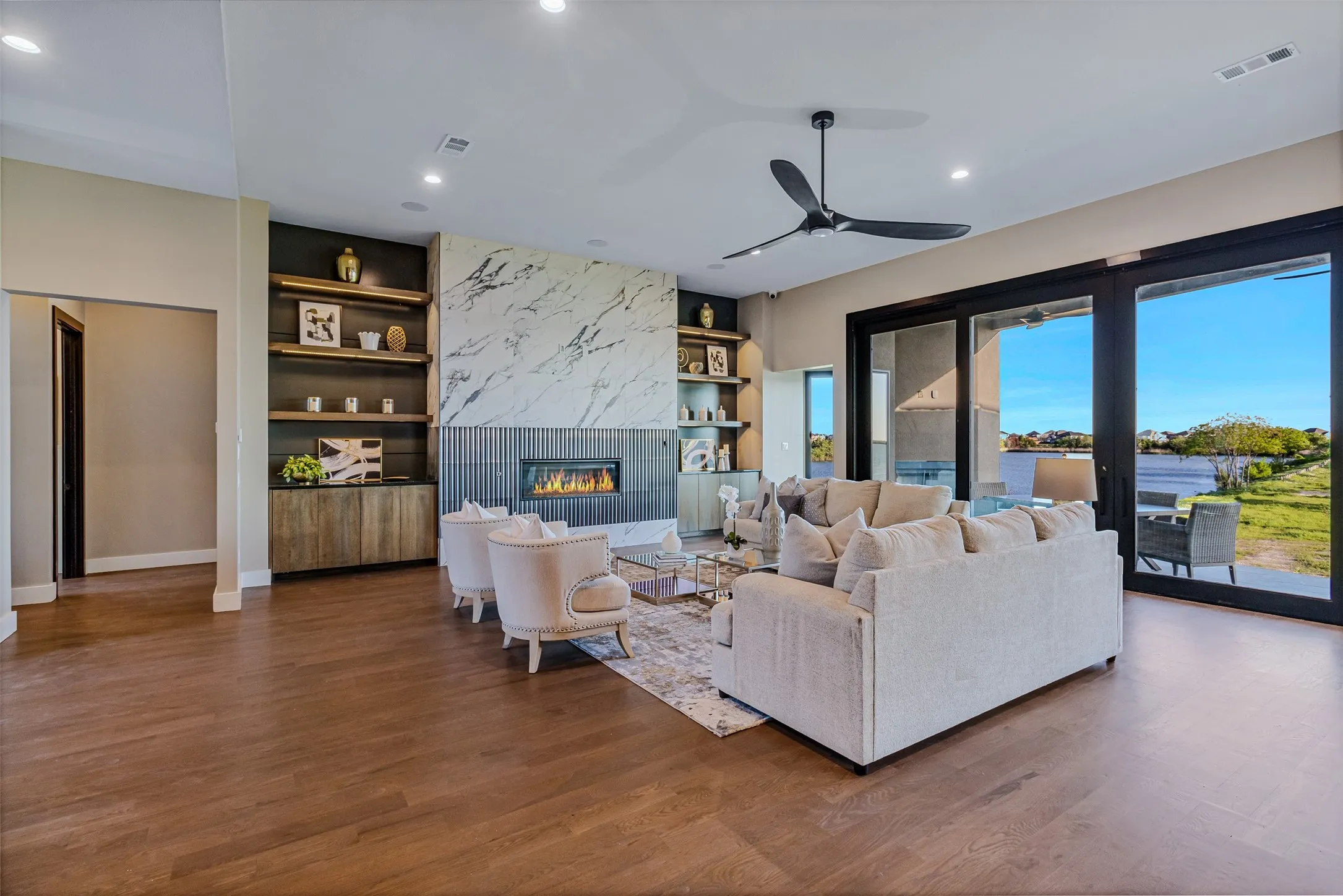 Spacious living area featuring wide-plank wood-finish flooring, a modern fireplace with a marble-look surround, built-in shelving, and large sliding glass doors opening to the outdoors