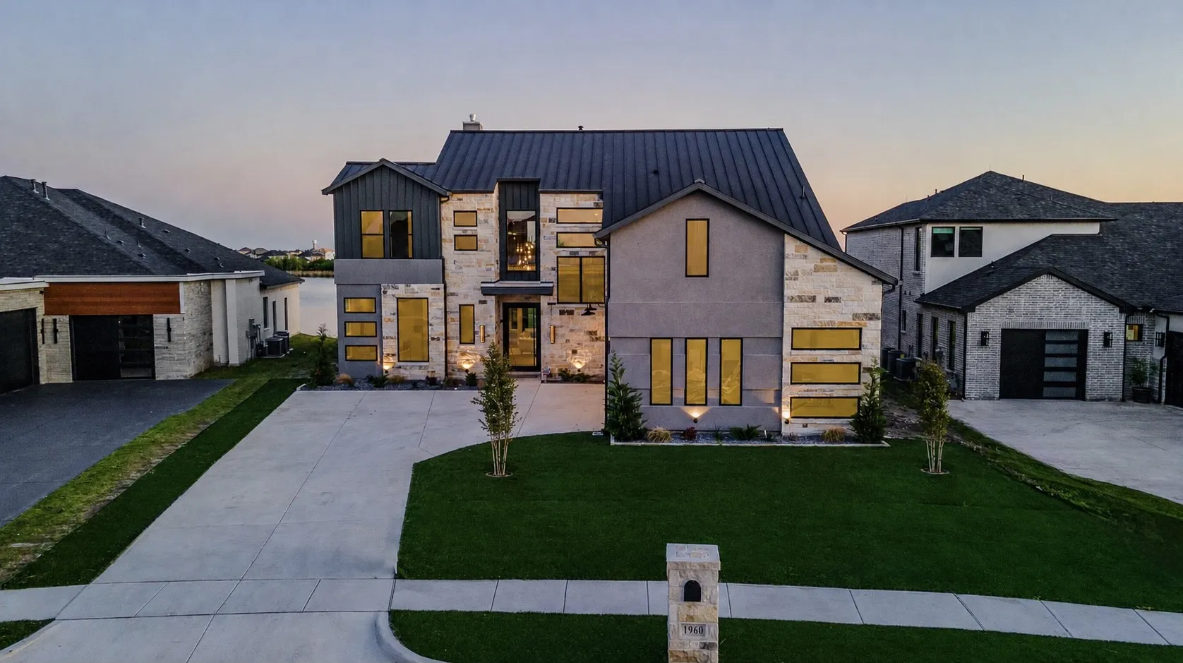 Modern two-story residence featuring a stone and stucco facade, a dark metal roof, and a prominent concrete driveway