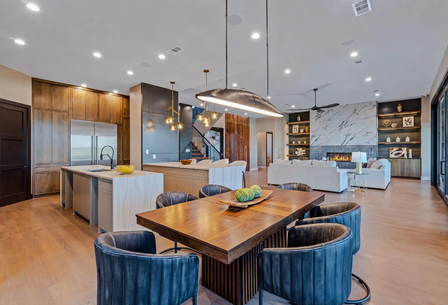 Open-concept living space featuring wood-finish flooring, a contemporary dining area with an oversized pendant light, and a kitchen with an island sink and integrated stainless steel appliances