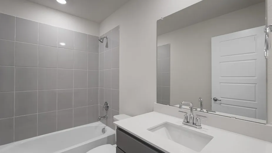 Bathroom featuring a white bathtub with light gray tile surround, sleek vanity with an integrated sink, polished chrome faucet, and a large wall-mounted mirror