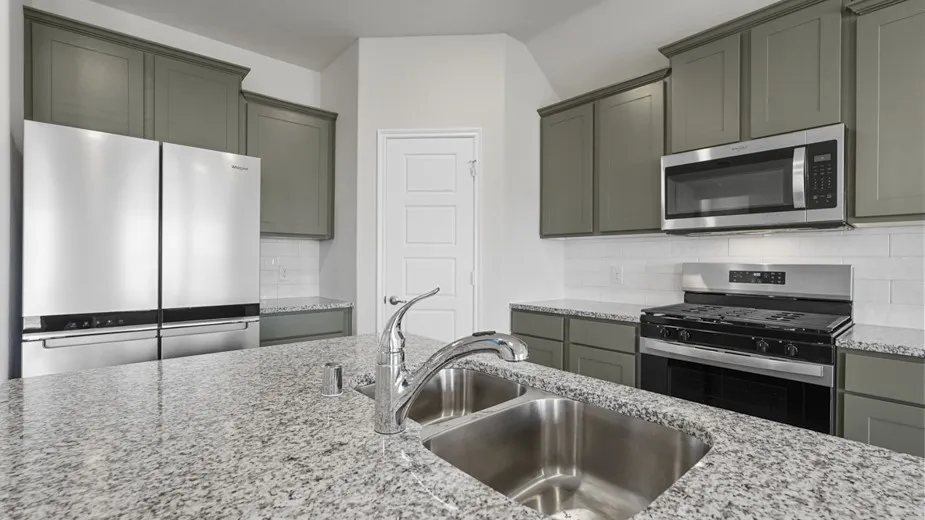 Kitchen featuring a double basin stainless steel sink, chrome faucet, granite countertops, sage cabinetry, and stainless steel appliances including a side-by-side refrigerator, microwave, and gas range