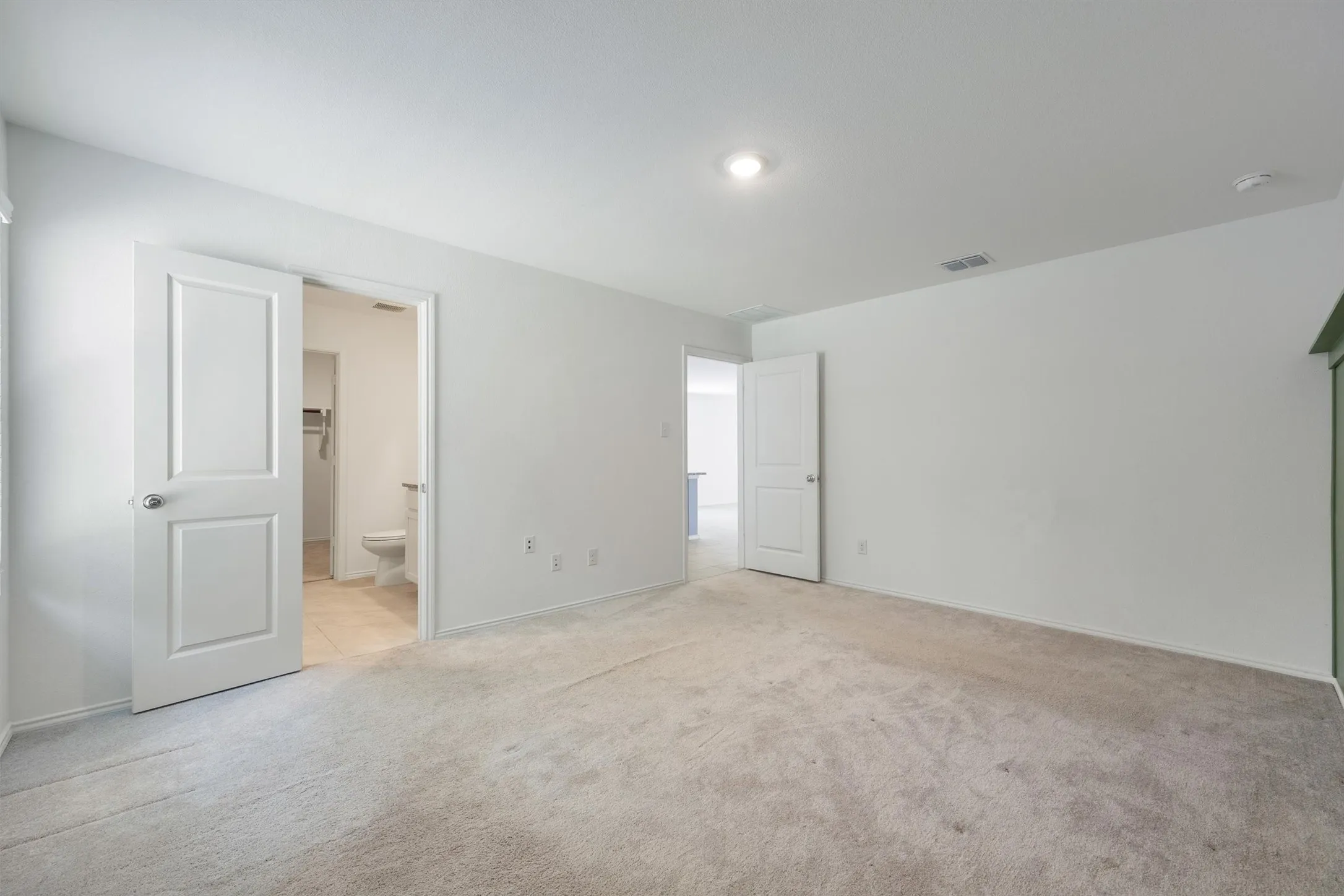 Carpeted room with a neutral color palette, featuring a recessed light fixture and a white paneled door