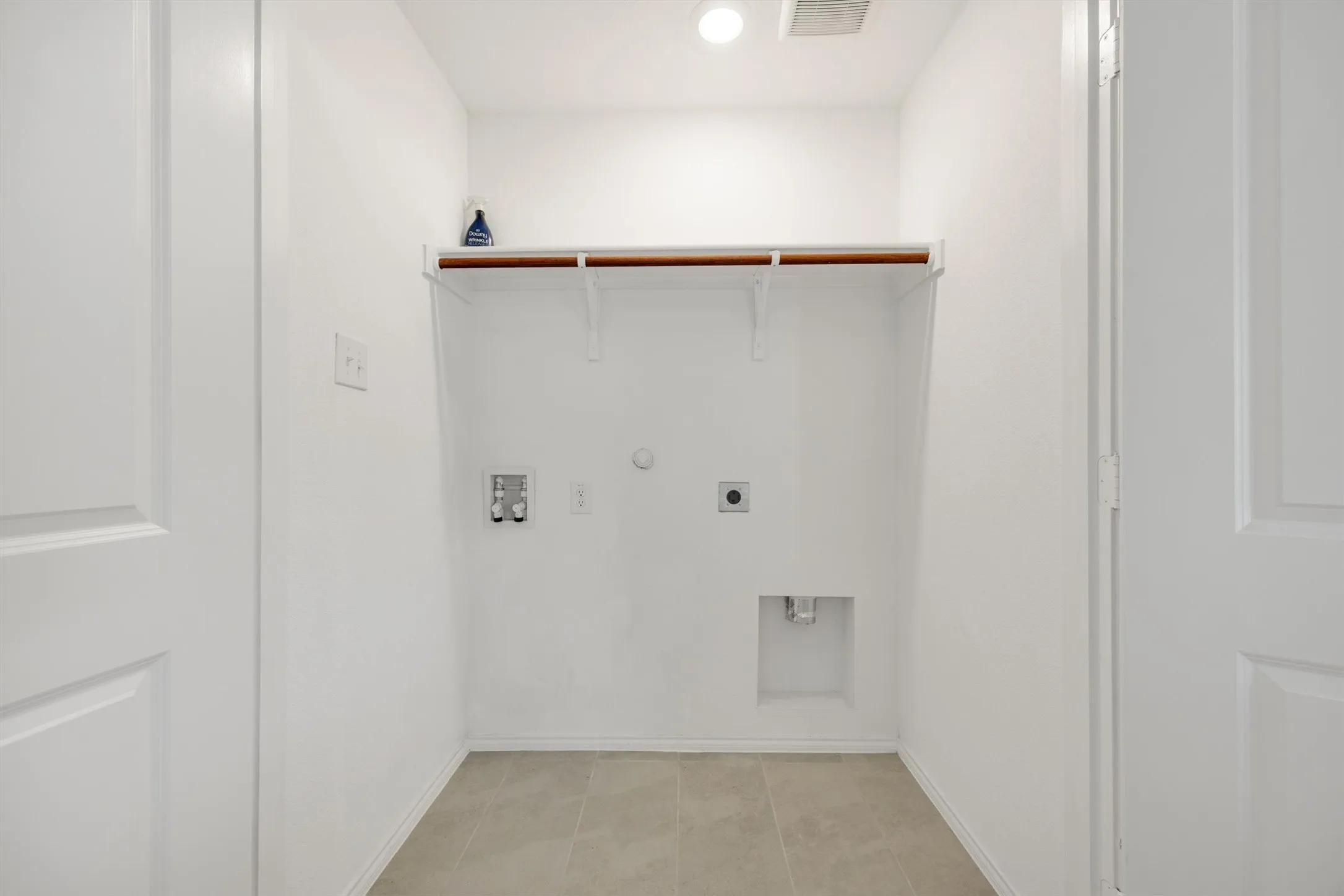 Dedicated utility area featuring a built-in shelf with hanging rod, light-toned tile flooring, and white walls