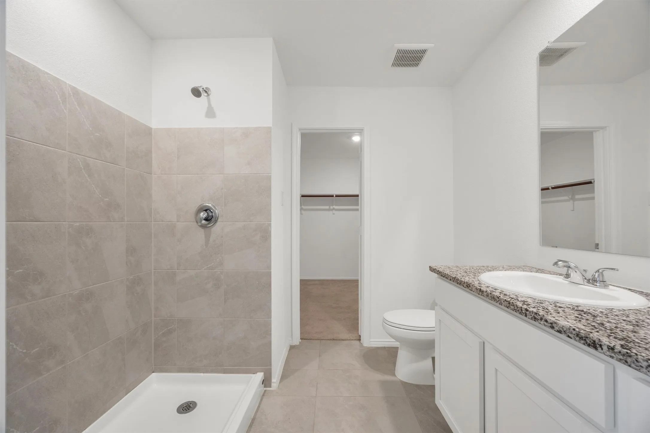Full bathroom featuring a walk-in shower with light-toned wall tile, a white vanity cabinet, a speckled countertop, a single basin sink, and an integrated mirror