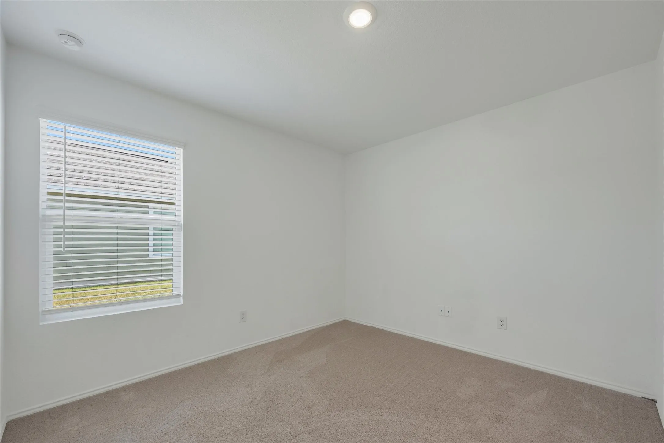 Neutral interior space featuring light-colored carpet, white walls, and a single window with blinds