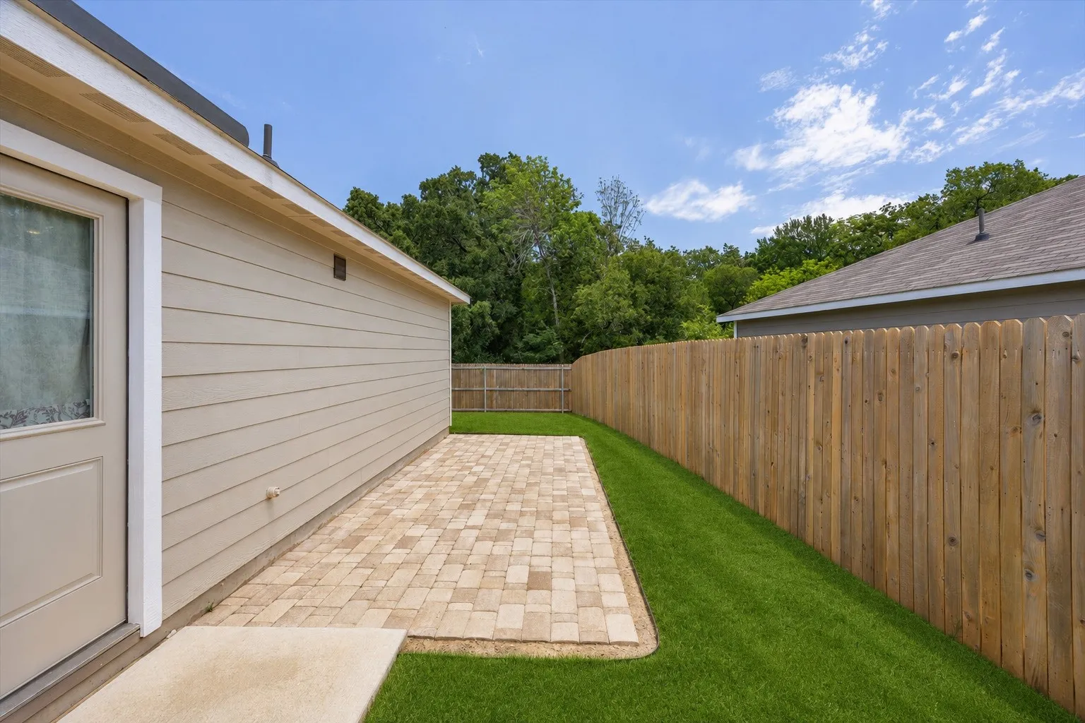 Outdoor living space featuring a textured paver patio, artificial turf, and a wood privacy fence