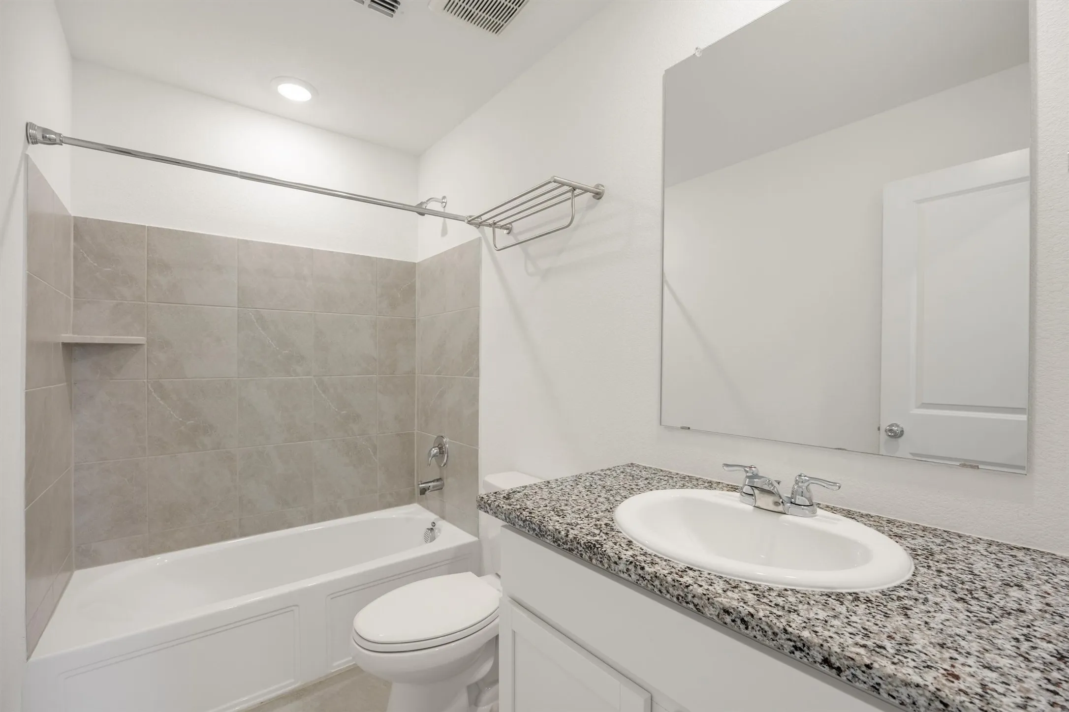 Bathroom featuring a white bathtub, tiled shower surround with built-in shelf, white vanity with speckled countertop, and a wall-mounted mirror