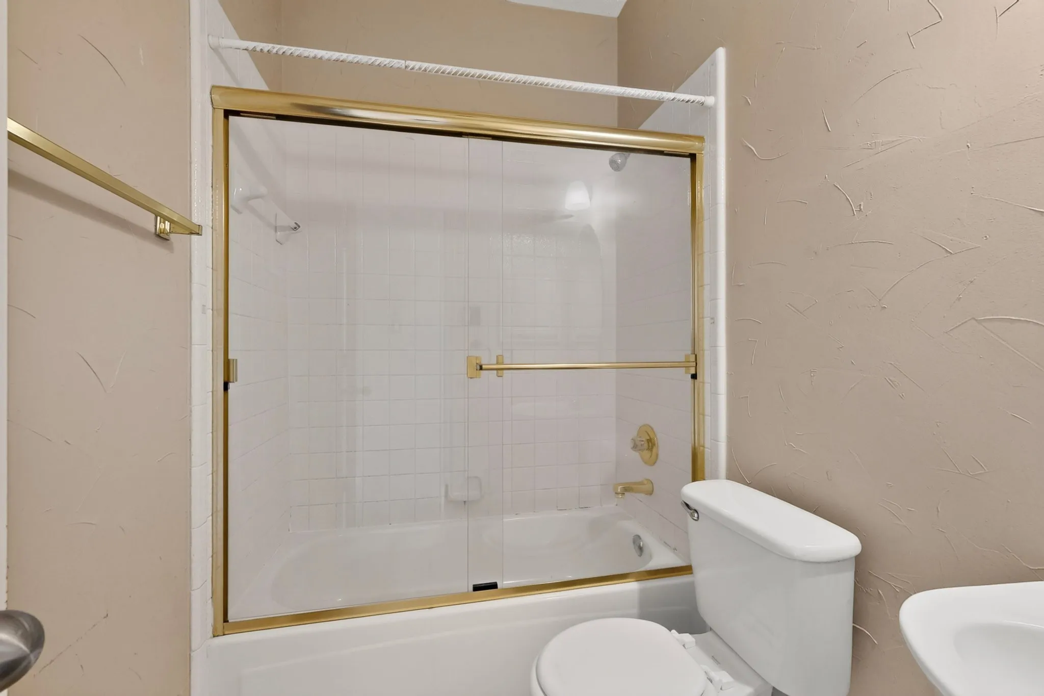 Bathtub with gold-tone framed sliding glass doors, white subway tile surround, and gold-tone fixtures