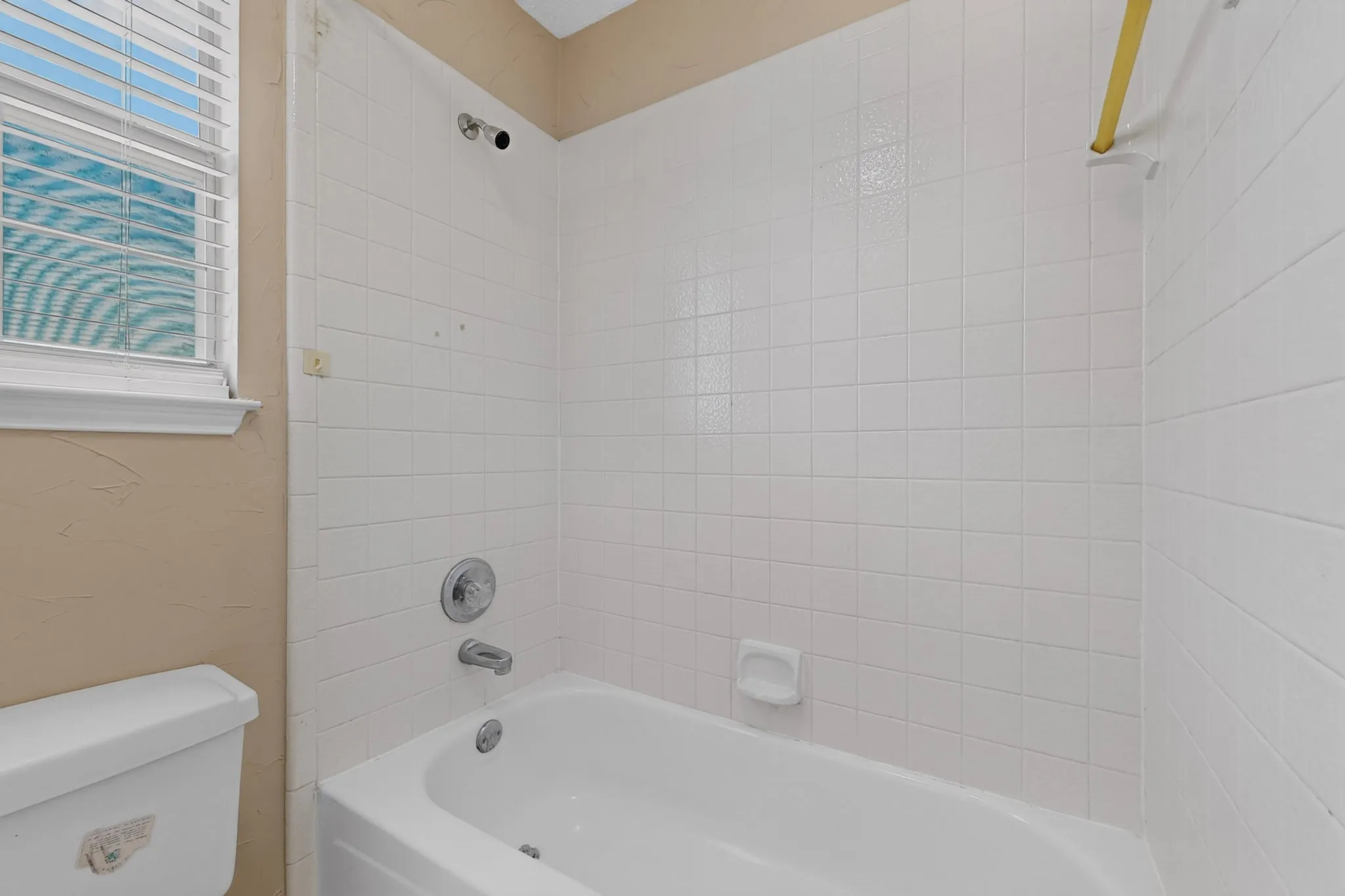 Bathtub with white tile surround, chrome fixtures, and a window with blinds