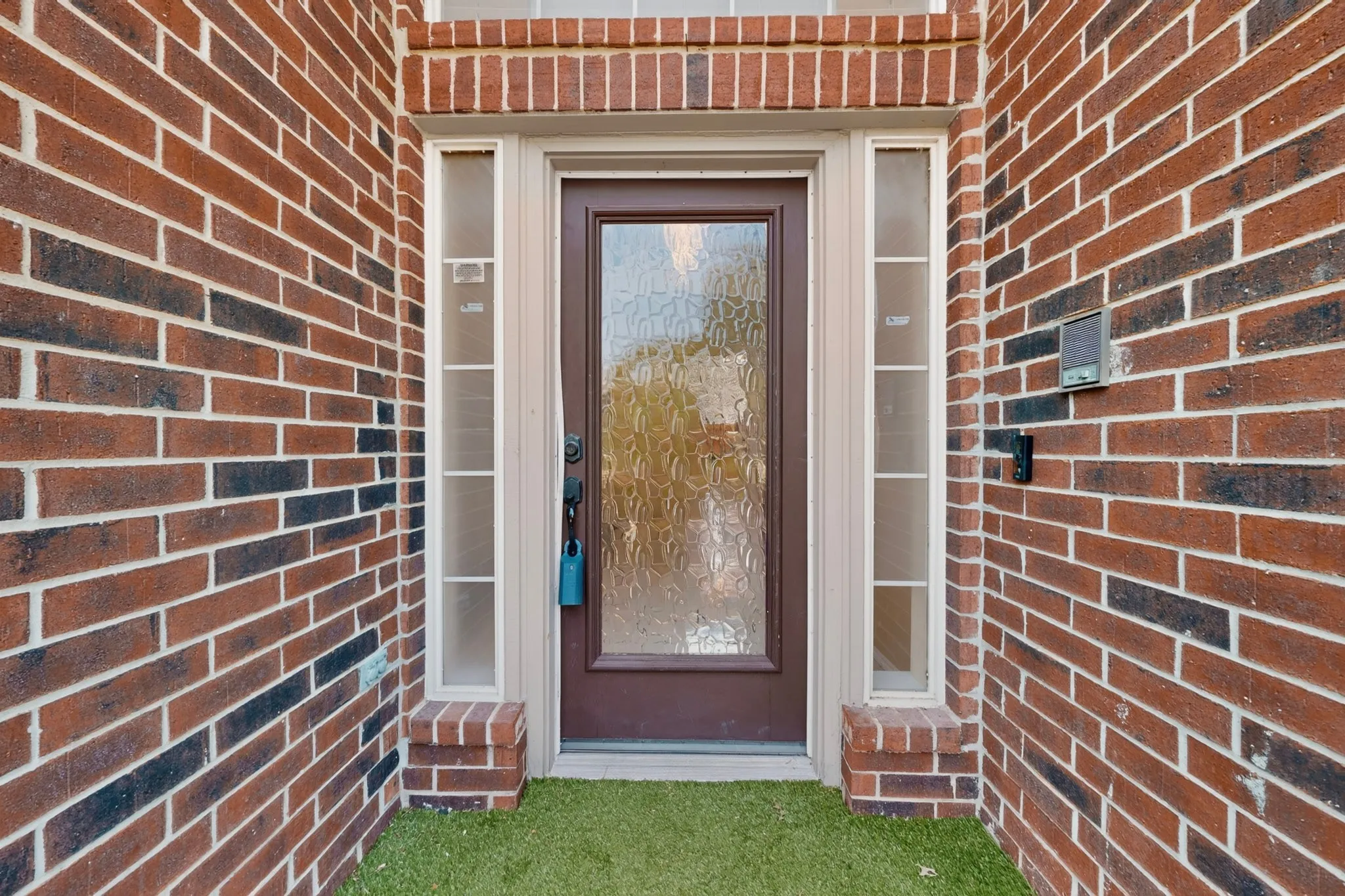 Welcoming entry featuring a dark-finish steel and glass door with sidelights, white trim framing, and brick exterior with varied warm tones