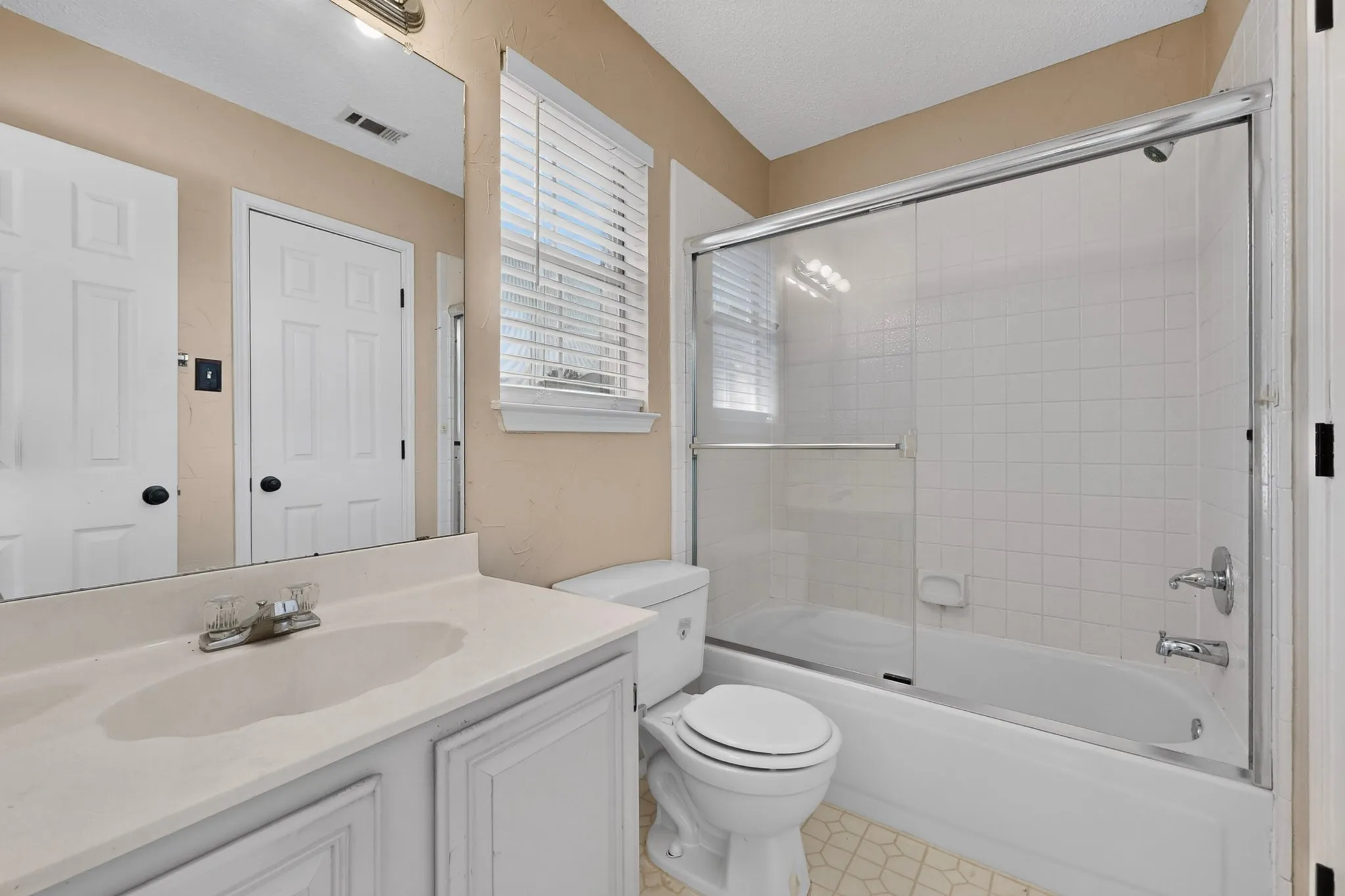 Bathroom featuring a vanity with an integrated sink, a built-in mirror, and a shower/tub combination with a sliding glass enclosure